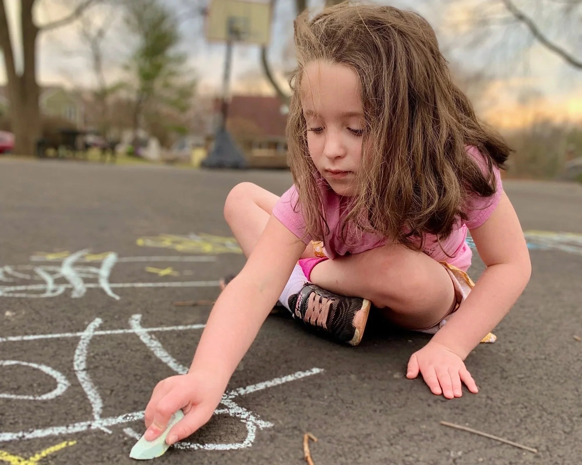 little girl draws on the ground and cement with sidewalk chalk in a photo by Erin E Gallagher Photography