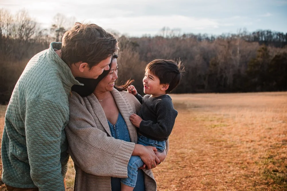 Pregnant mom holding toddler son while dad stands nearby, all are laughing with each other during a sunset fall  session in Richmond, VA by Erin E Gallagher Photography