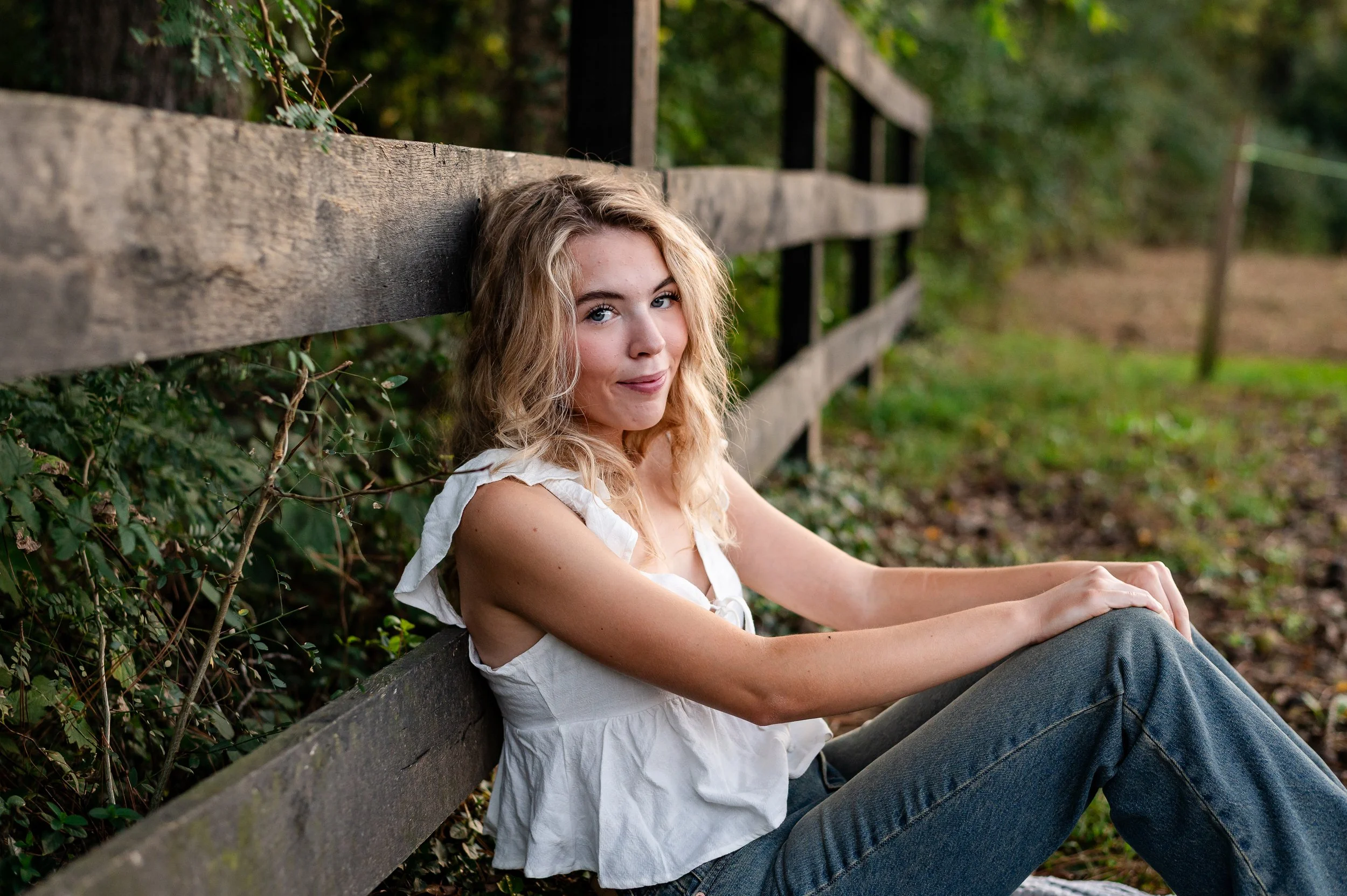 senior girl sitting against a fence during a senior session by Erin E Gallagher Photography Foxhaven Farms