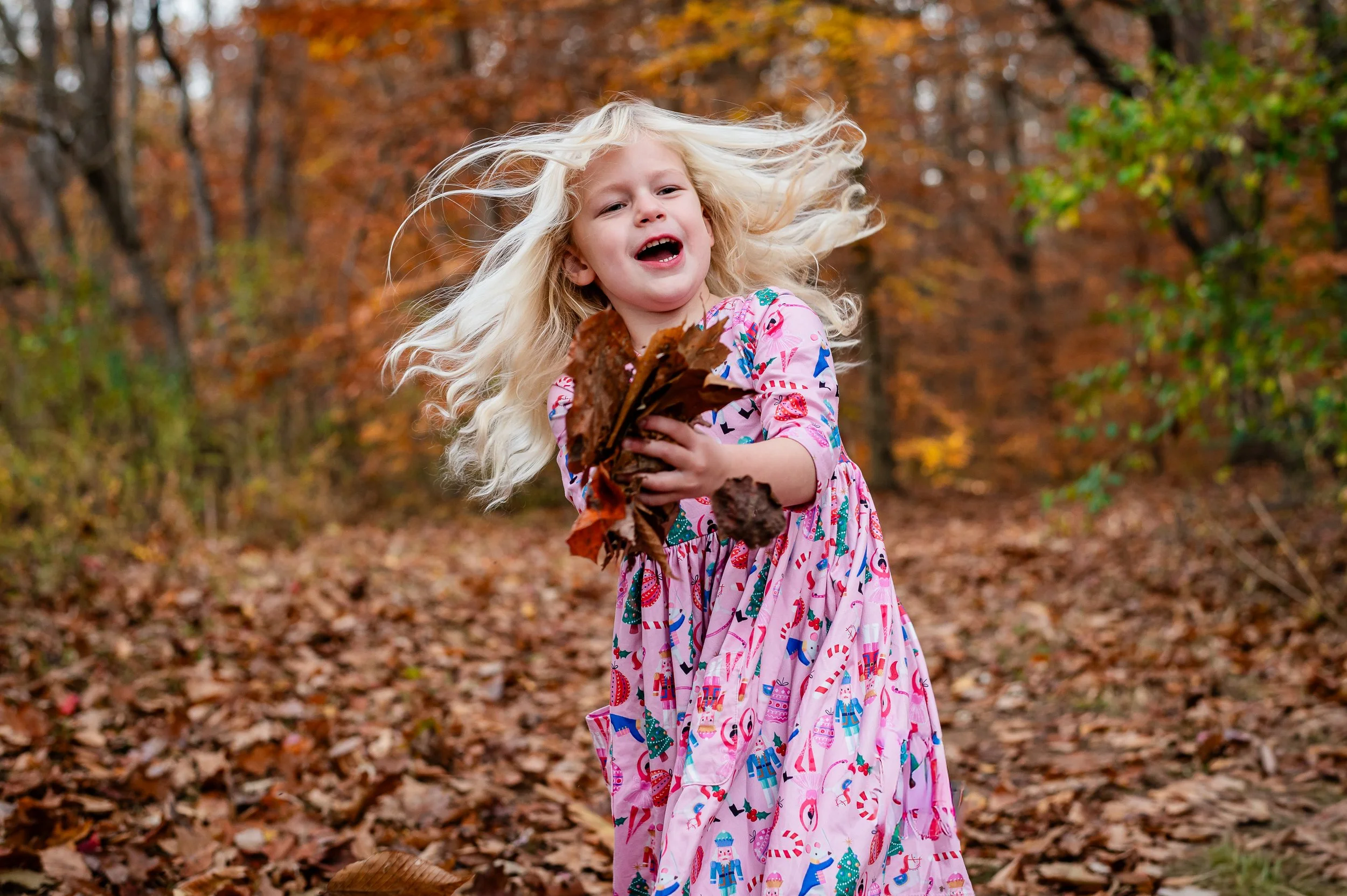 little girl playing in the leaves and laughing during outdoor fall family pictures