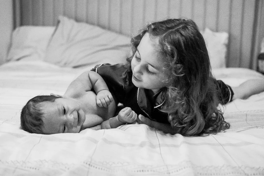 At-home newborn session in Harrisonburg, Virginia — big sister meeting her baby sibling for the first time during cozy in-home photography session.
