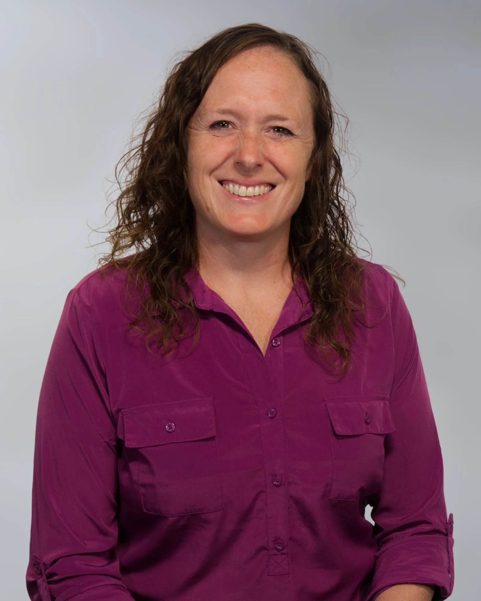 Black and white photo of a smiling woman with long wavy hair, wearing a striped top and cardigan.