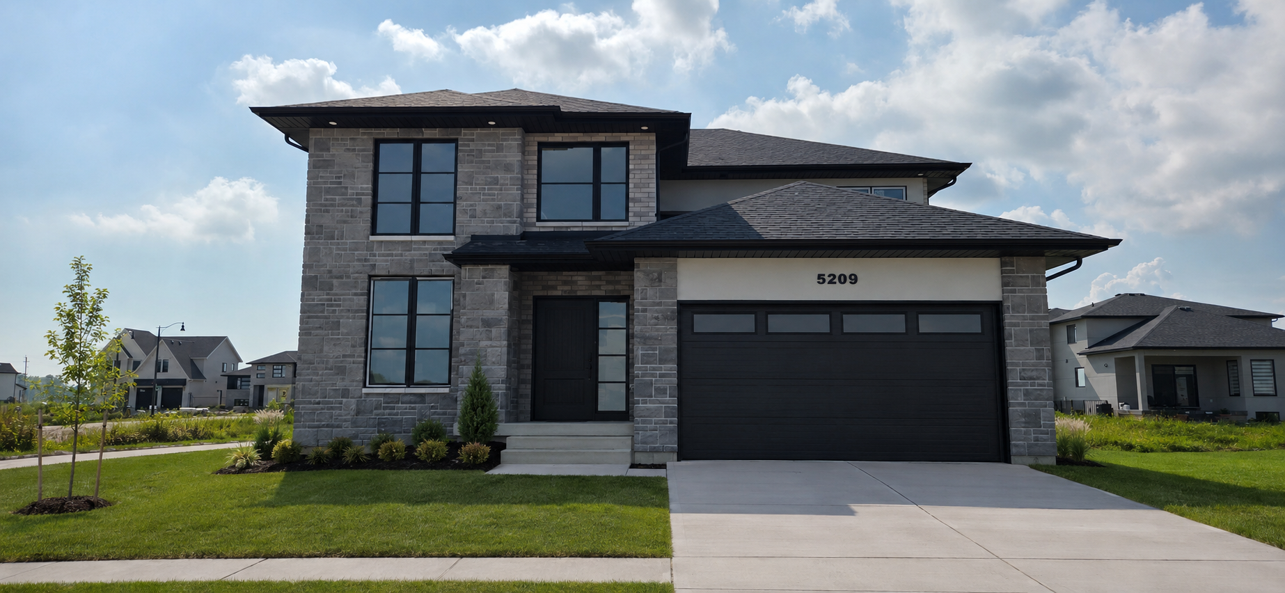 Front view of a modern two-story house with stone and white exterior, grey shingle roof, black window frames, and attached garage, on a sunny day with a well-maintained lawn.