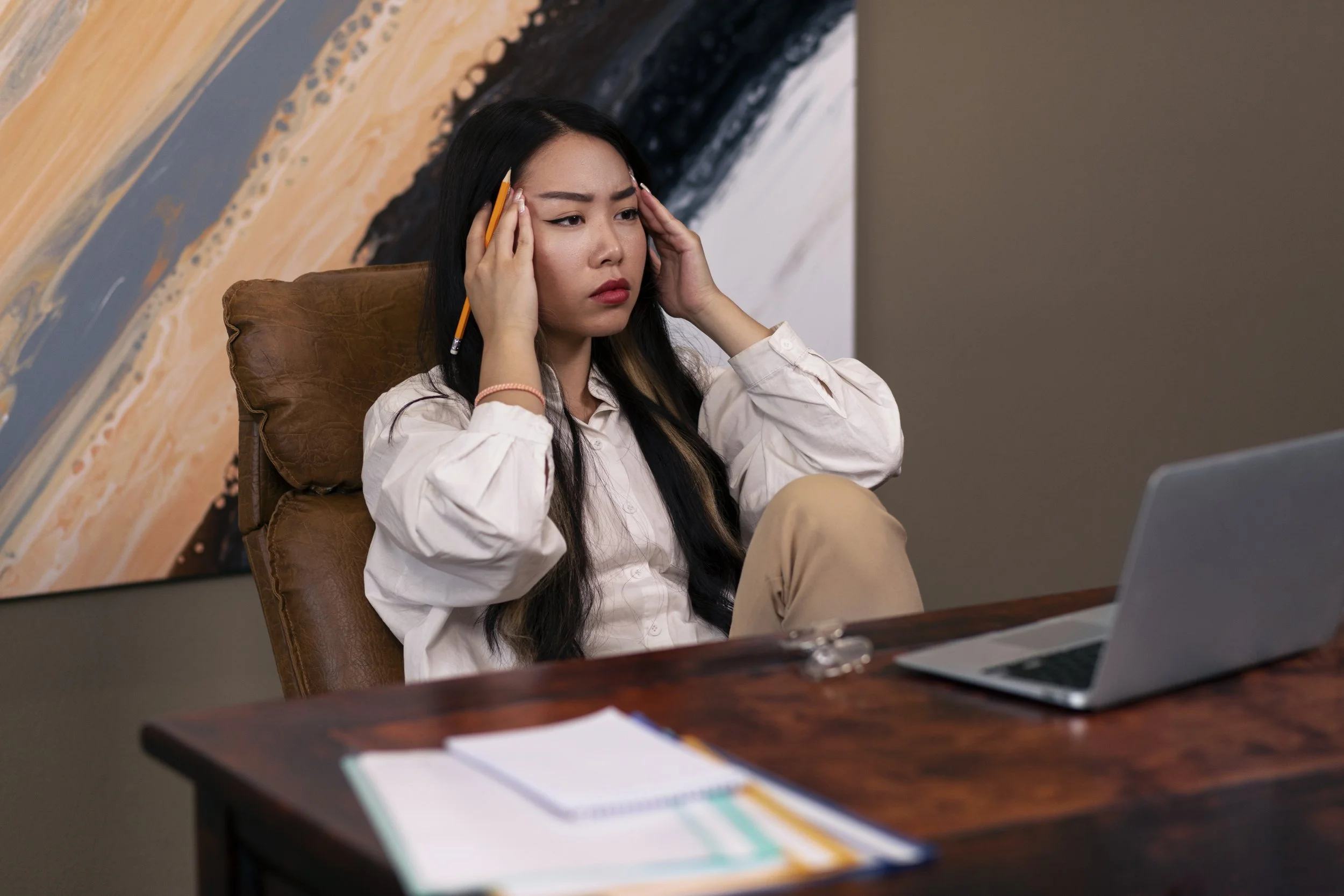 A woman at a desk, head in hands, appears overwhelmed by marketing challenges as a therapist.