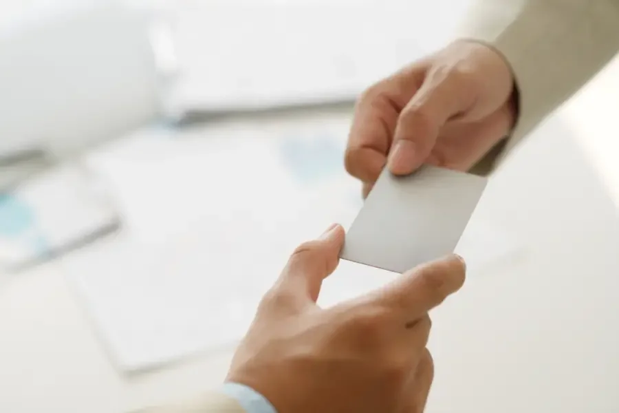 A businessman hands a business card to another person, symbolizing networking and trust in professional relationships.