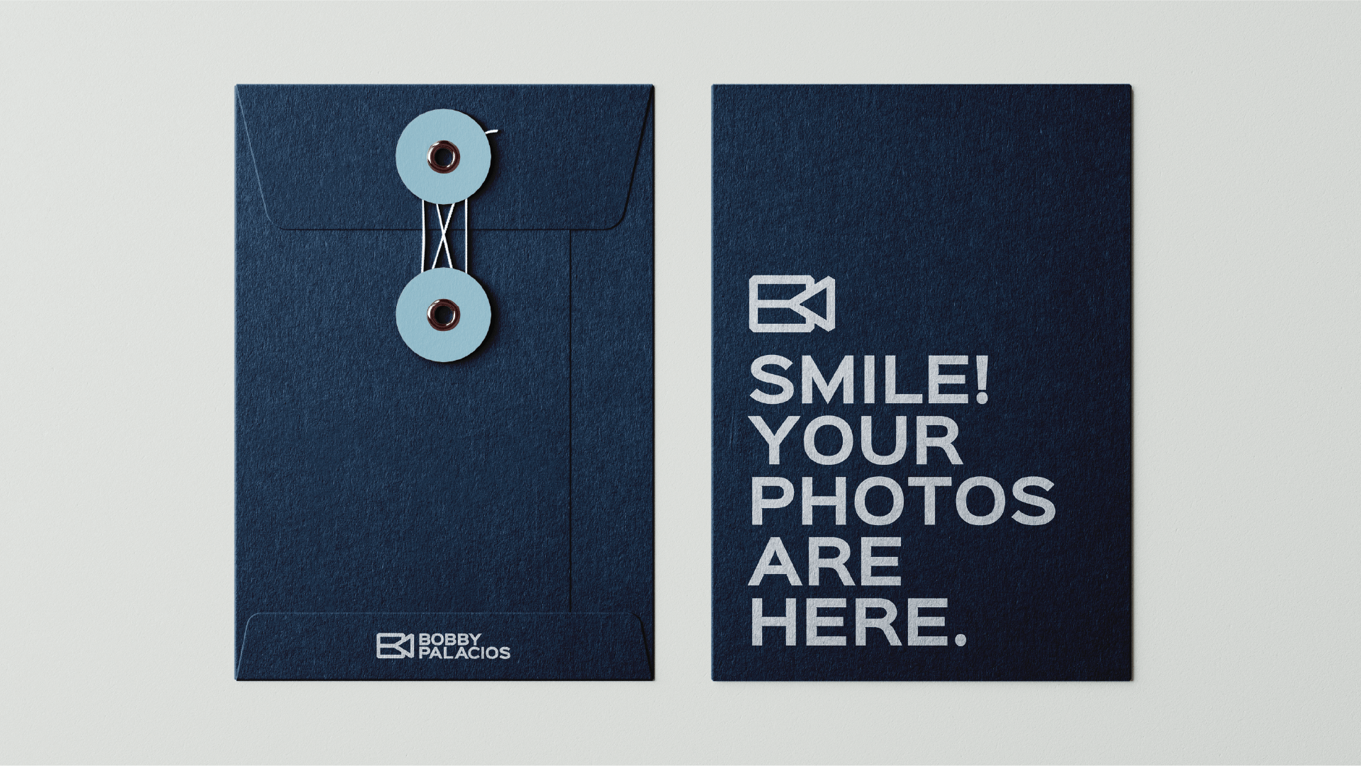 Image of a navy blue envelope with a circular closure on the left and a sign on the right that says, "Smile! Your photos are here."