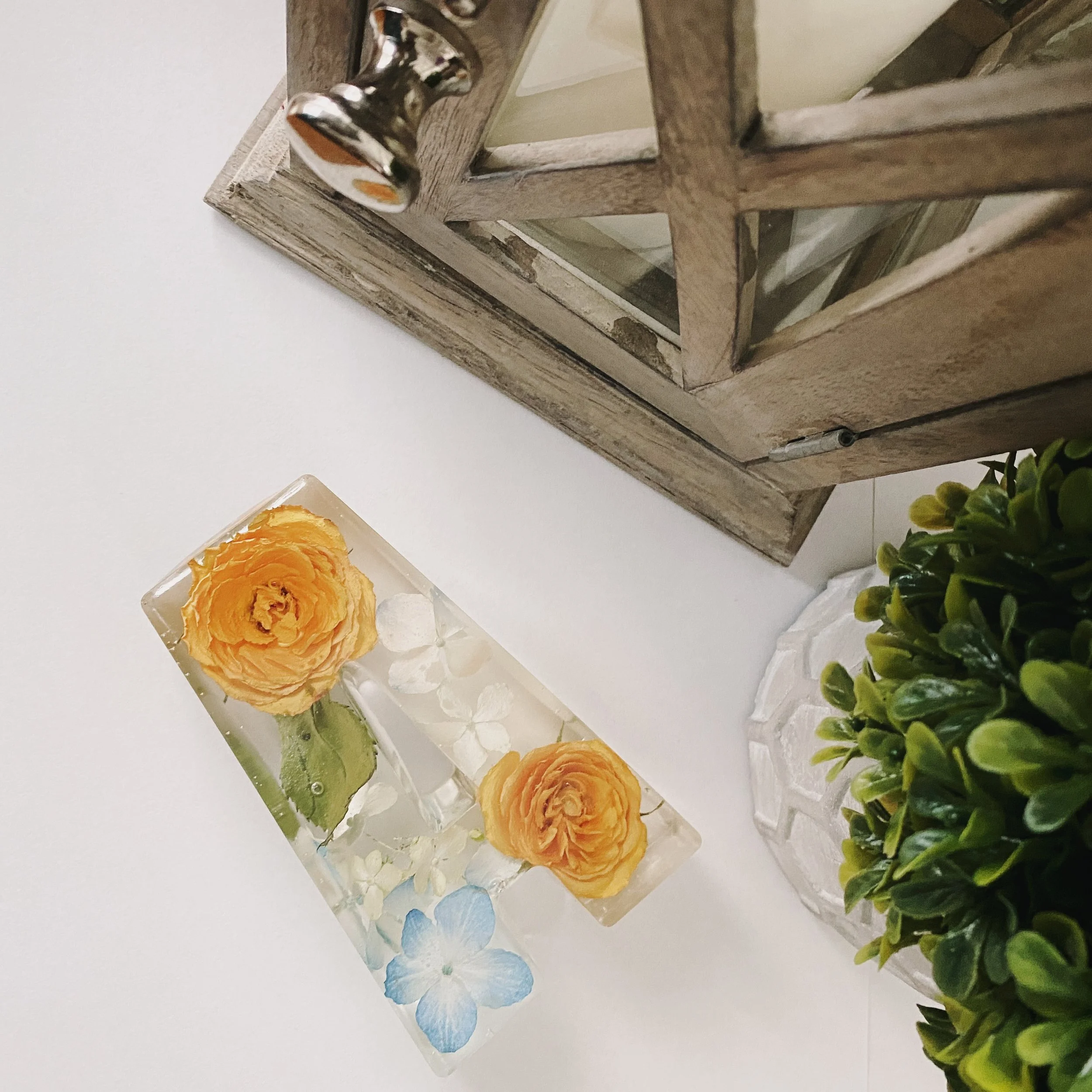 Resin letter A with embedded flowers on a white surface near a wooden decorative box and a small plant.