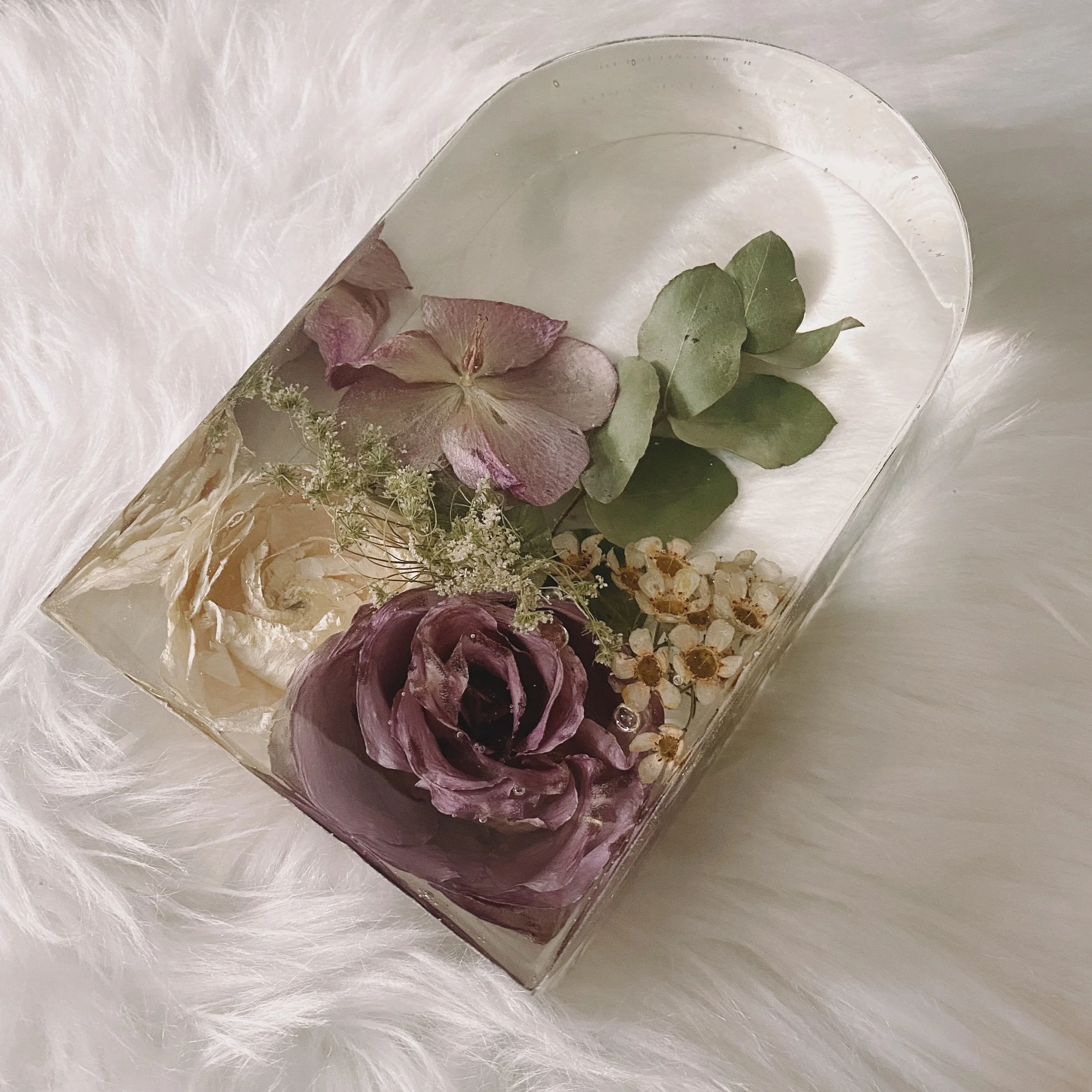 Decorative resin block with embedded flowers and leaves on a soft white surface.