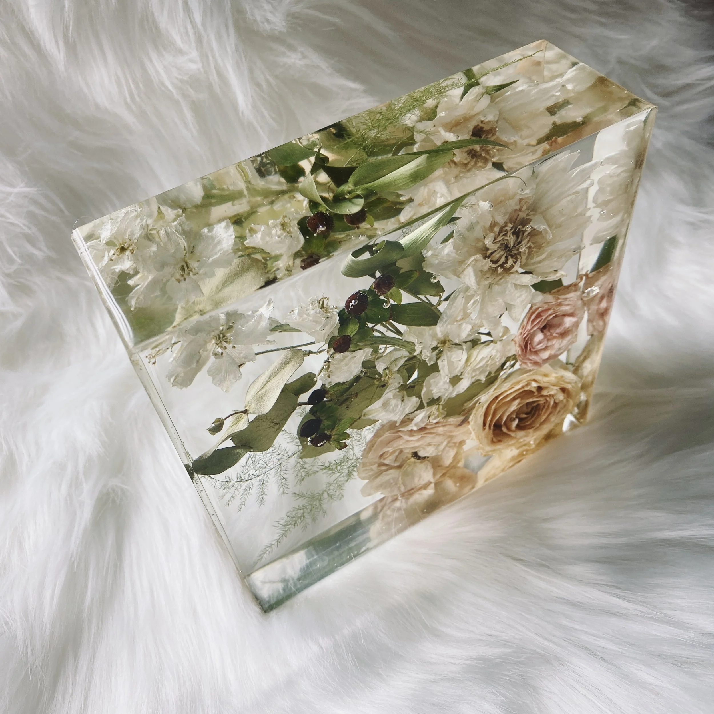 A block of clear resin encasing dried flowers and greenery, displayed on a soft white fur surface.