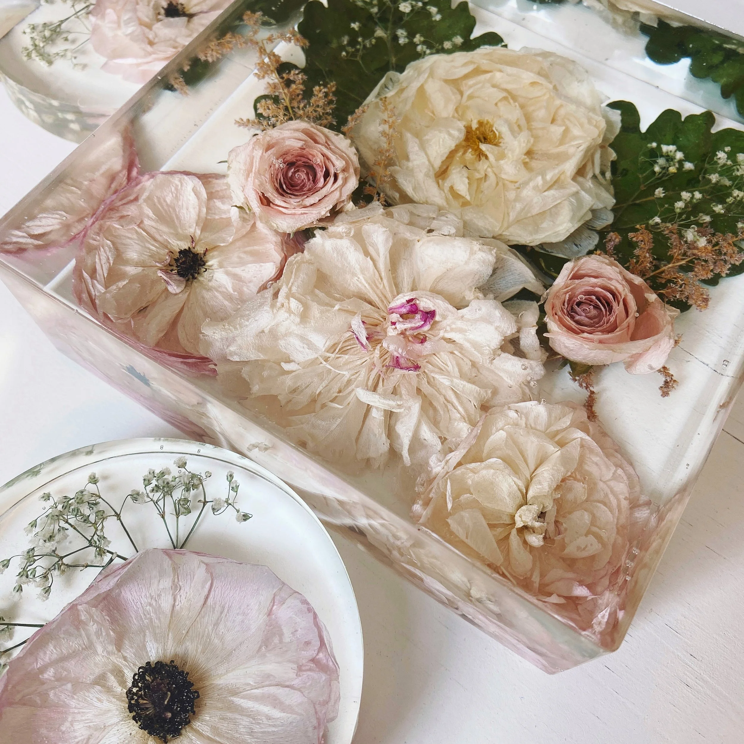 Dried flowers preserved in clear resin, including roses and other blooms, displayed in square and round molds.