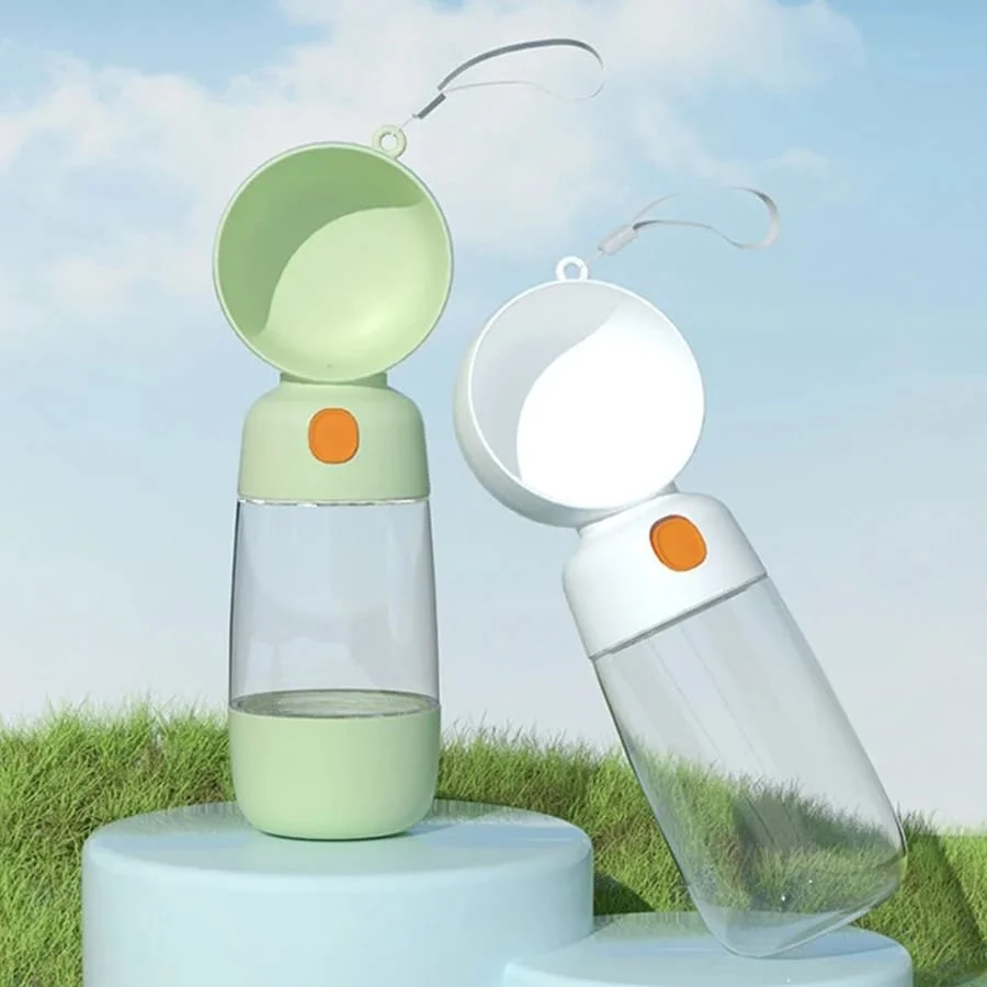 Two small, portable mist spray fans with spray bottles, one in green and one in white, positioned outdoors on a grassy surface with a blue sky background.