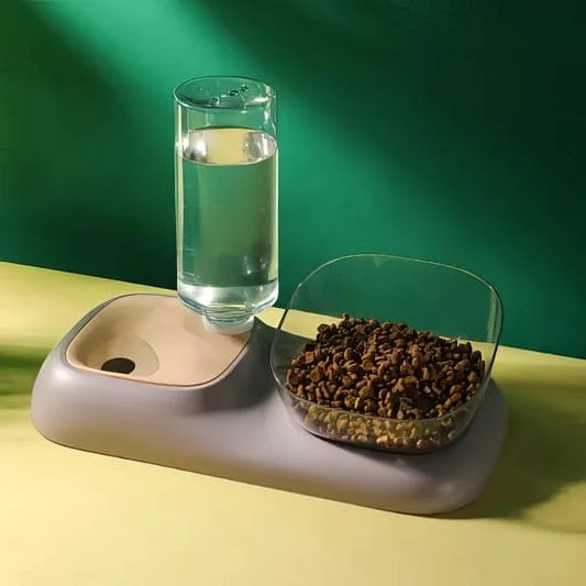 A glass of water with a lemon slice, a bowl of dry pet food, and a digital pet water fountain on a light-colored surface with a green background.