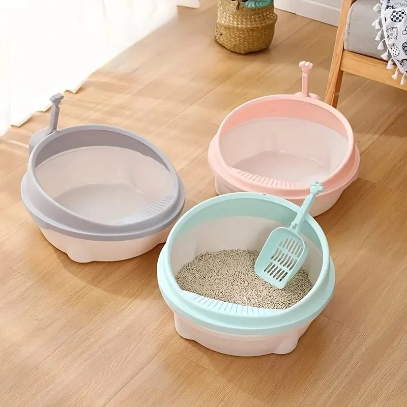 Three colorful cat litters boxes with scoops on a wooden floor, with a basket and a chair nearby.