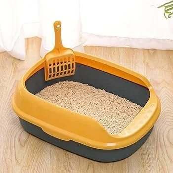 A yellow and black cat litter box with a scoop, on a wooden floor near a white curtain.
