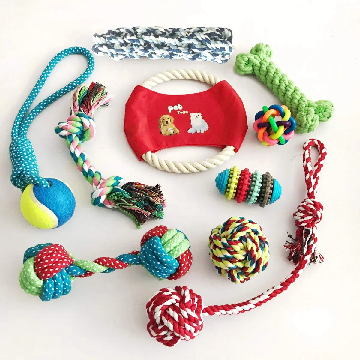 Collection of colorful dog toys including ropes, a tennis ball, a fabric ball, a rubber ball, a tug toy, and a treat dispenser, arranged on a white surface.