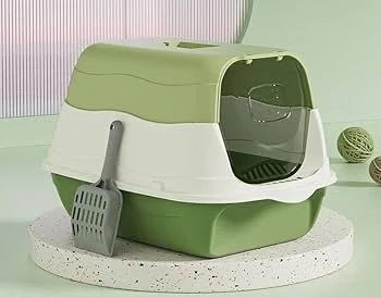 Green and white enclosed cat litter box with a small shovel attached, placed on a white speckled surface.