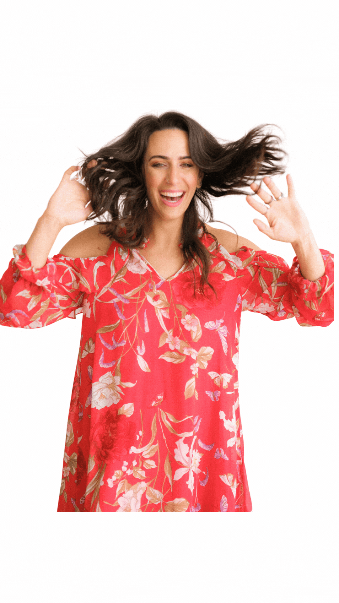 Woman in a floral cold-shoulder red dress smiling with hands raised, hair moving, on a white background.