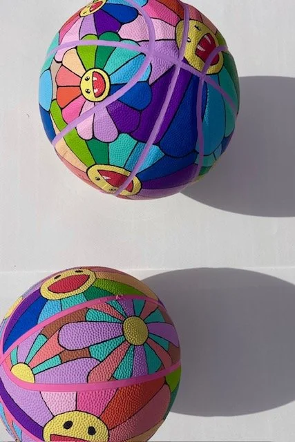 Colorful fabric-covered ball with cartoon smiley face and flower patterns, shown from above and side, casting shadows on a white background.