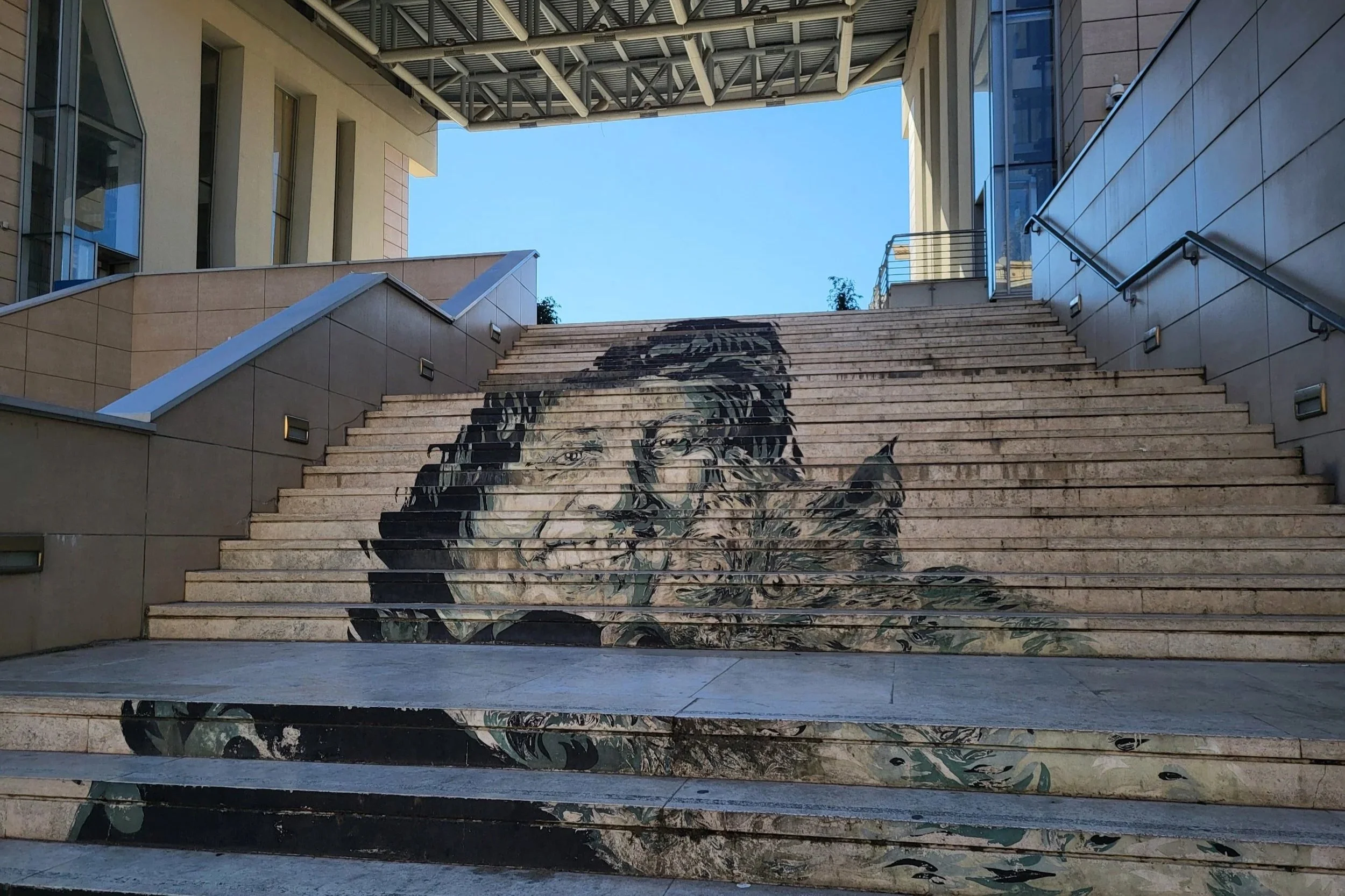 Picture of outside stairs at Aula Studio Trionfale, painting of an old lady at the sides of the stairs.