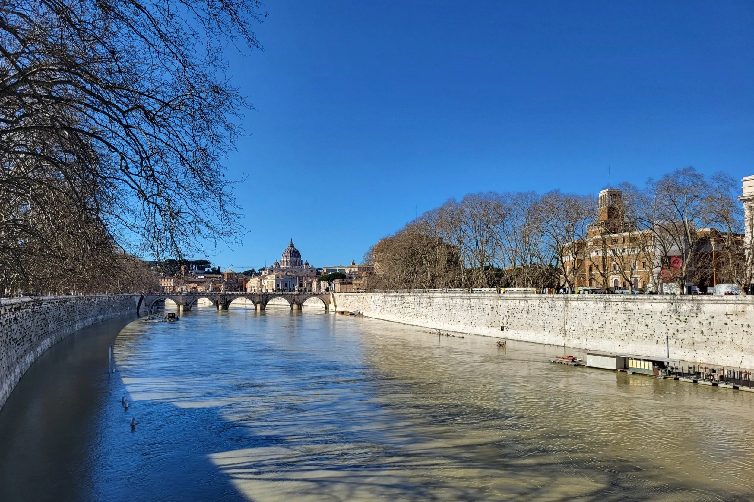 View of the river in Rome with the Vatican in the distance with a blue sky.