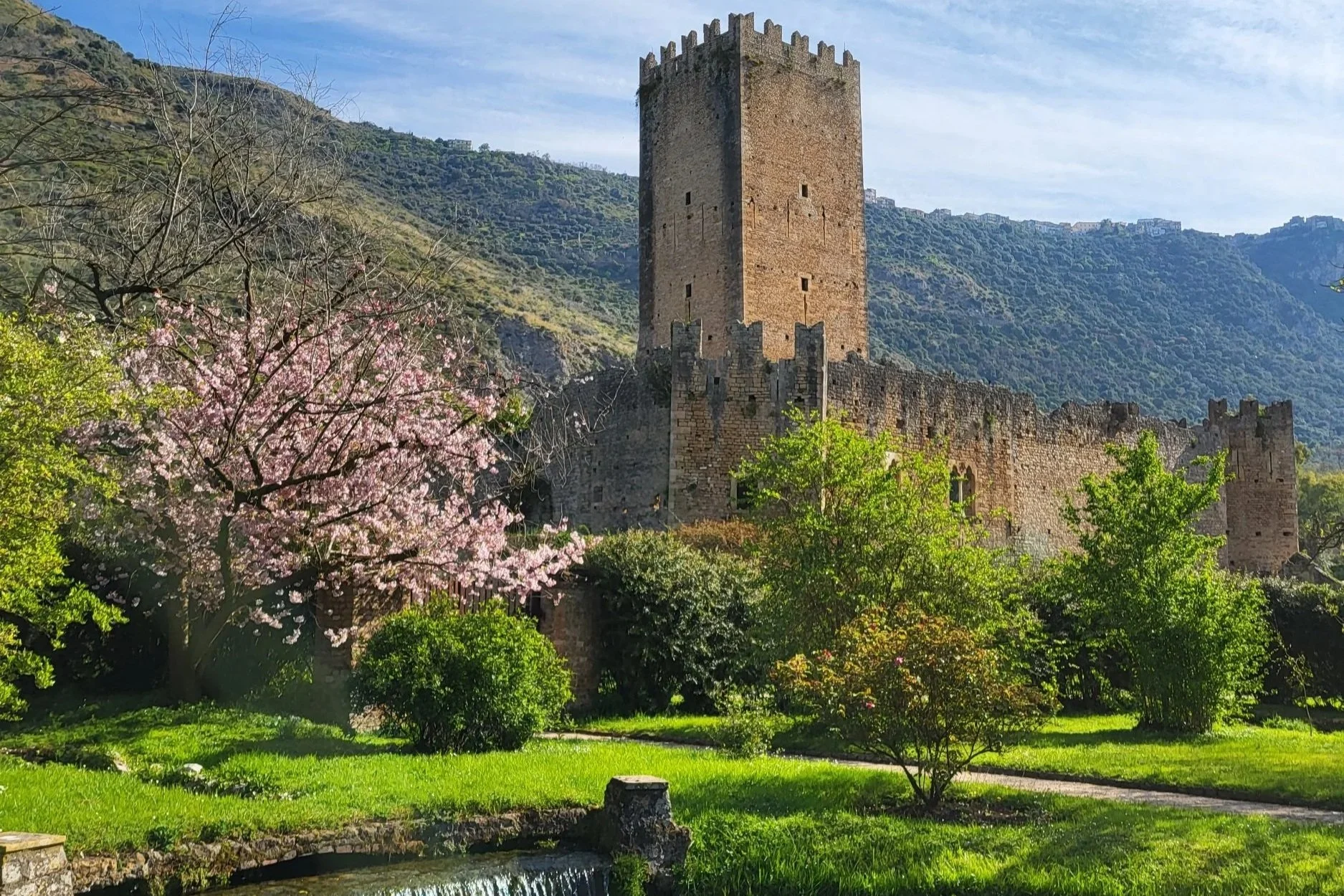 River and pink blossom tree in front of an ancient castle tower in Giardino di Ninfa