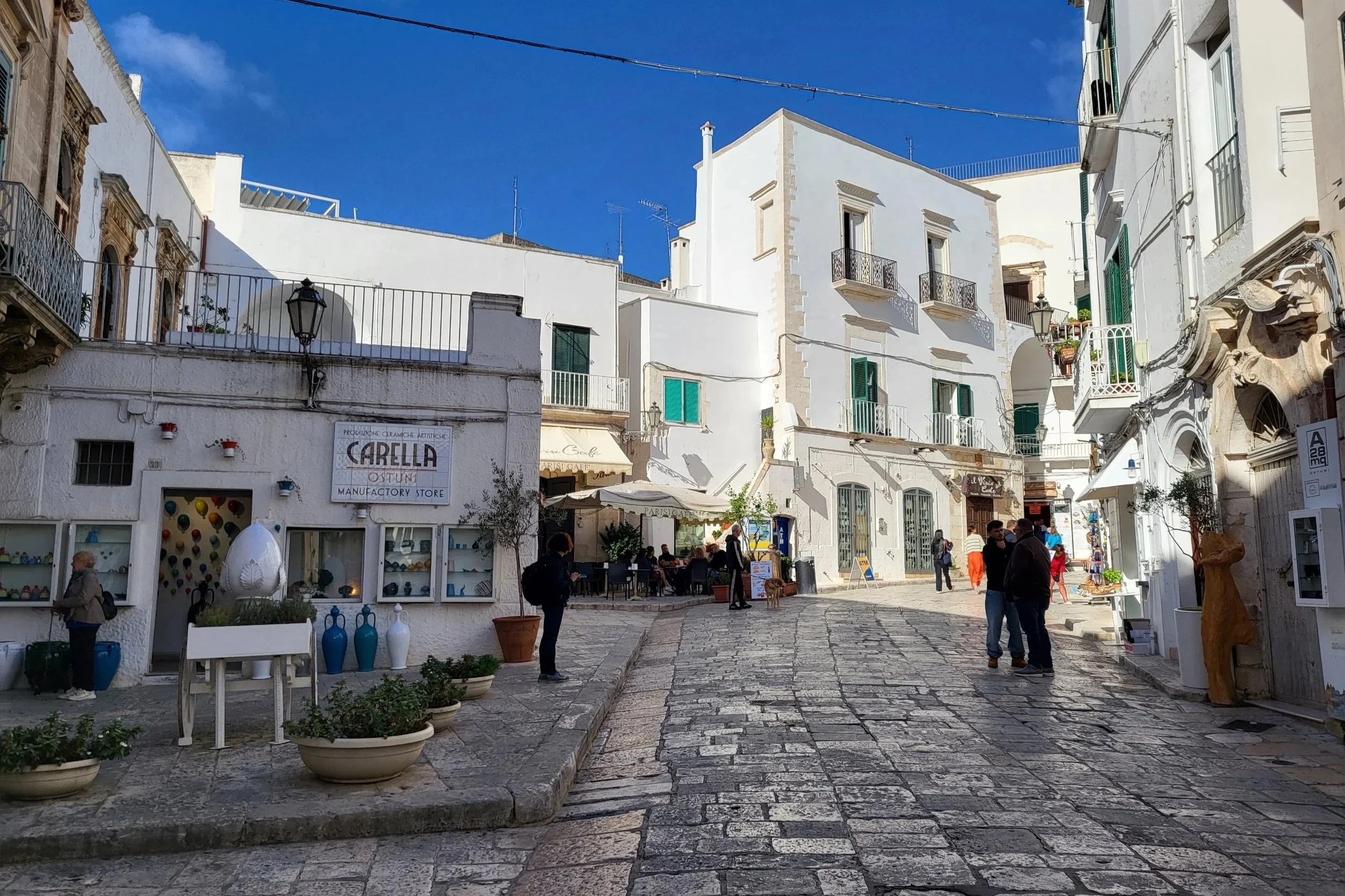 Charming street in Ostuni, Puglia, Italy, lined with shops, cafes, and white buildings.