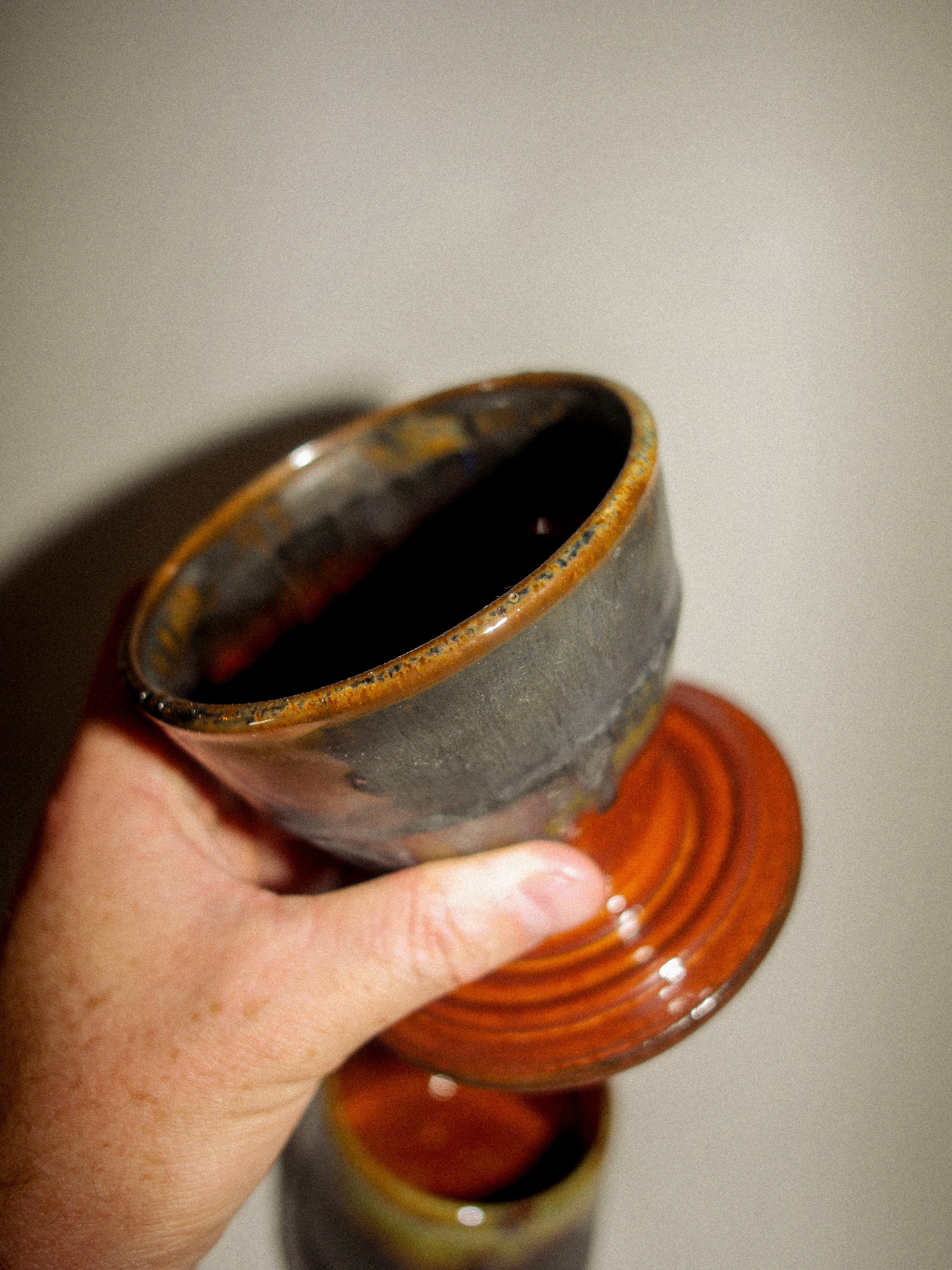 A person holding a ceramic goblet with a brown glazed rim, part of a stack of similar goblets, against a plain background.