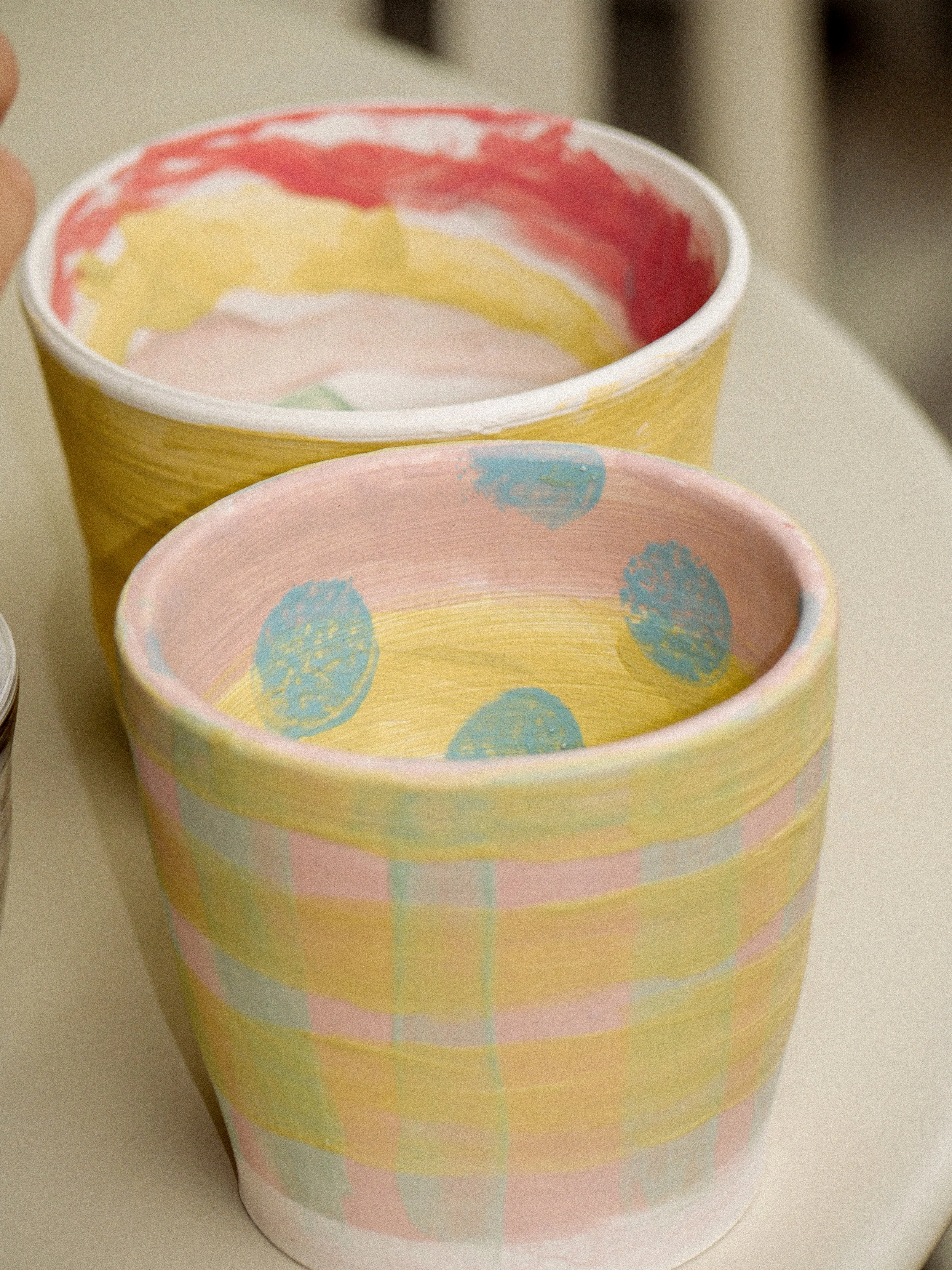 Colorful pastel-patterned paper cups with pink, yellow, and blue designs on a light surface.