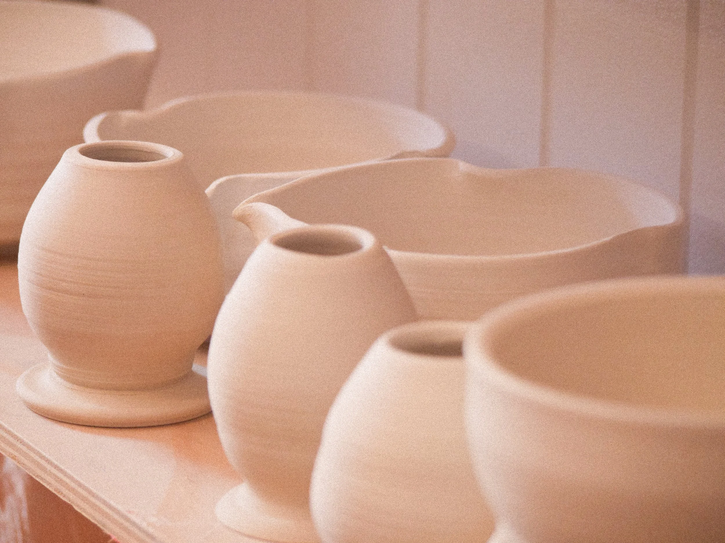 Multiple unfinished white ceramic vases with rounded shapes and wide openings on a wooden shelf, in a pottery studio.