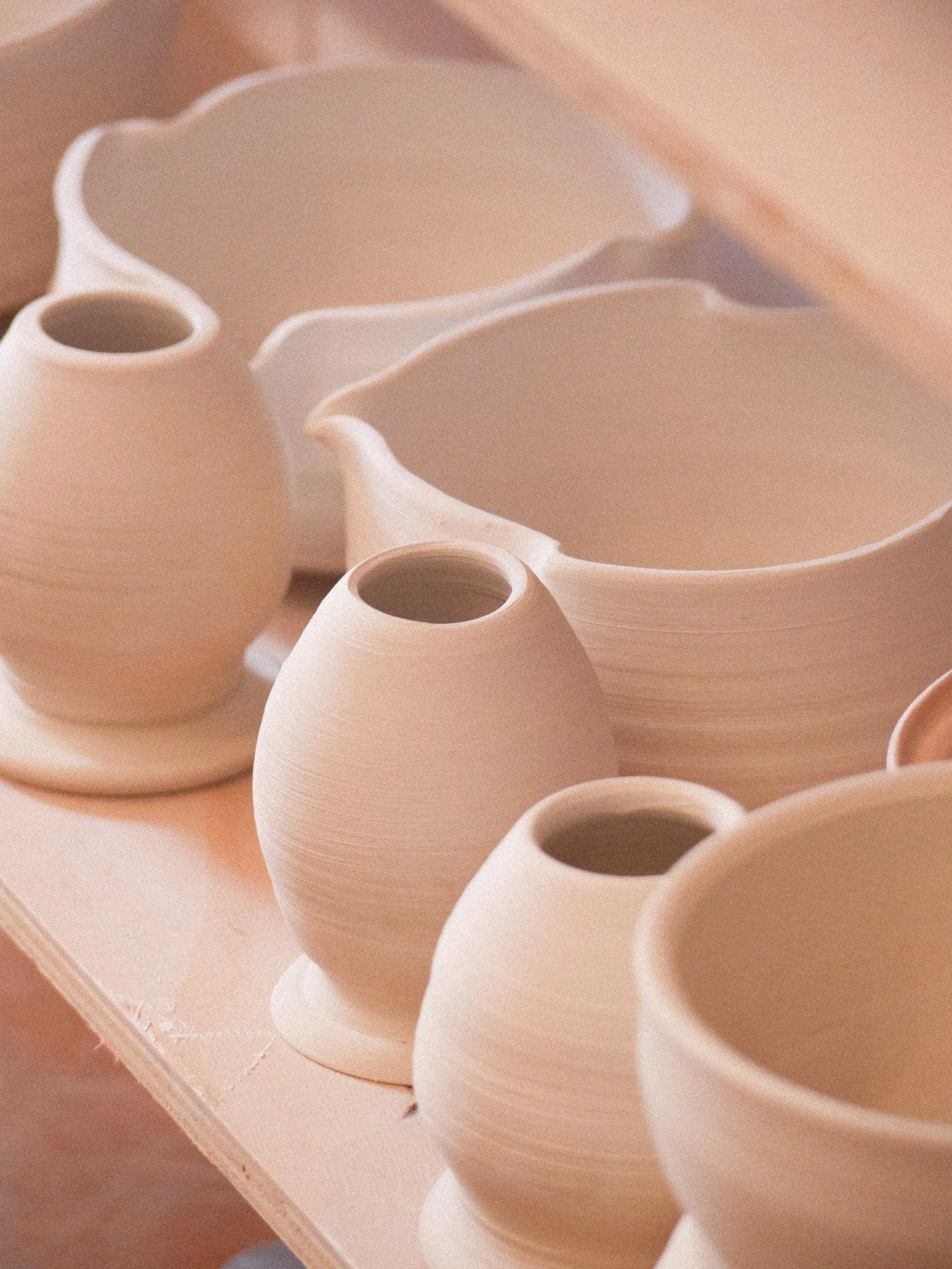 Several unglazed, cream-colored ceramic vases and bowls placed on a wooden surface in a pottery studio.