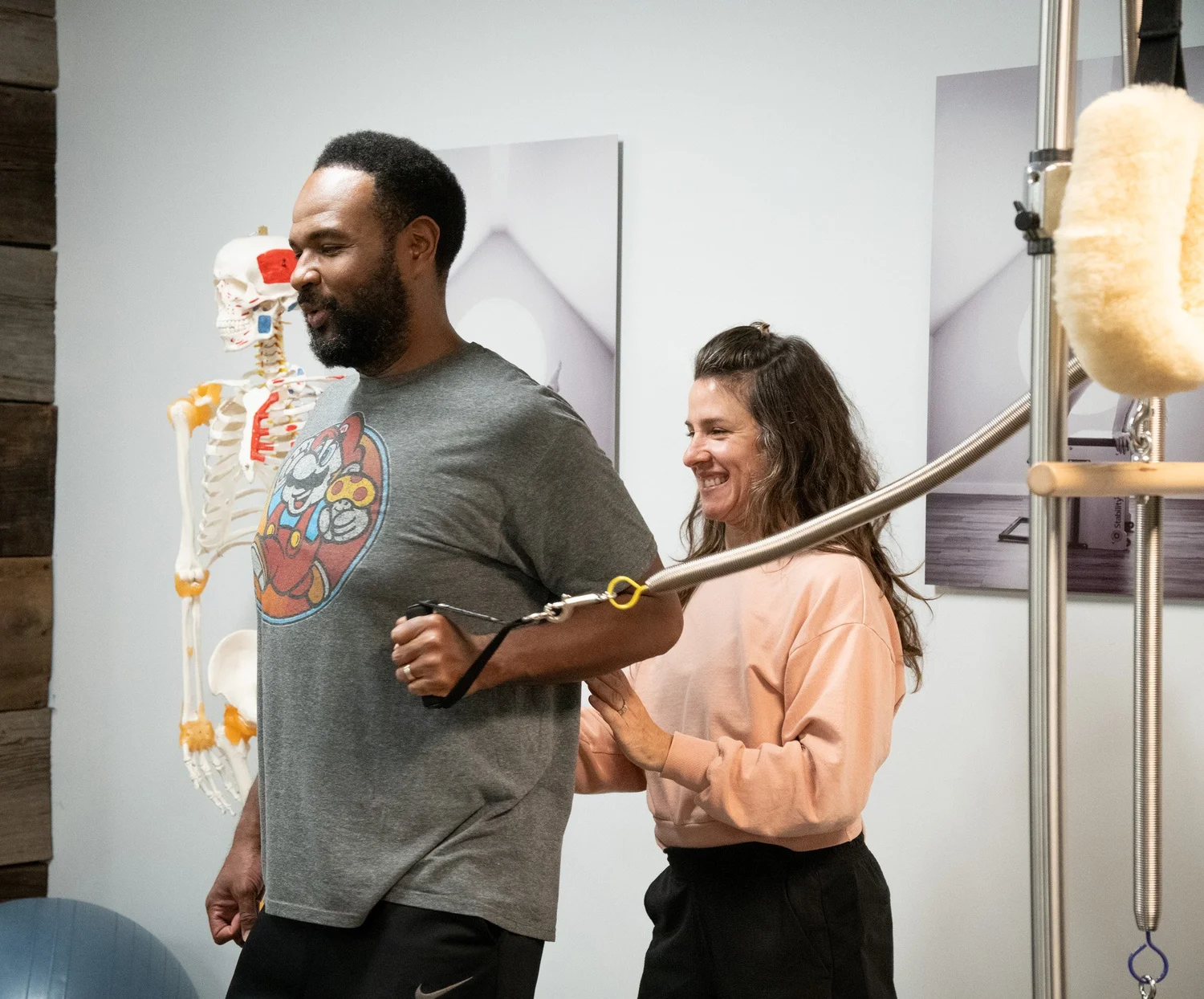 An RF client practicing standing Pilates with a smiling instructor beside him