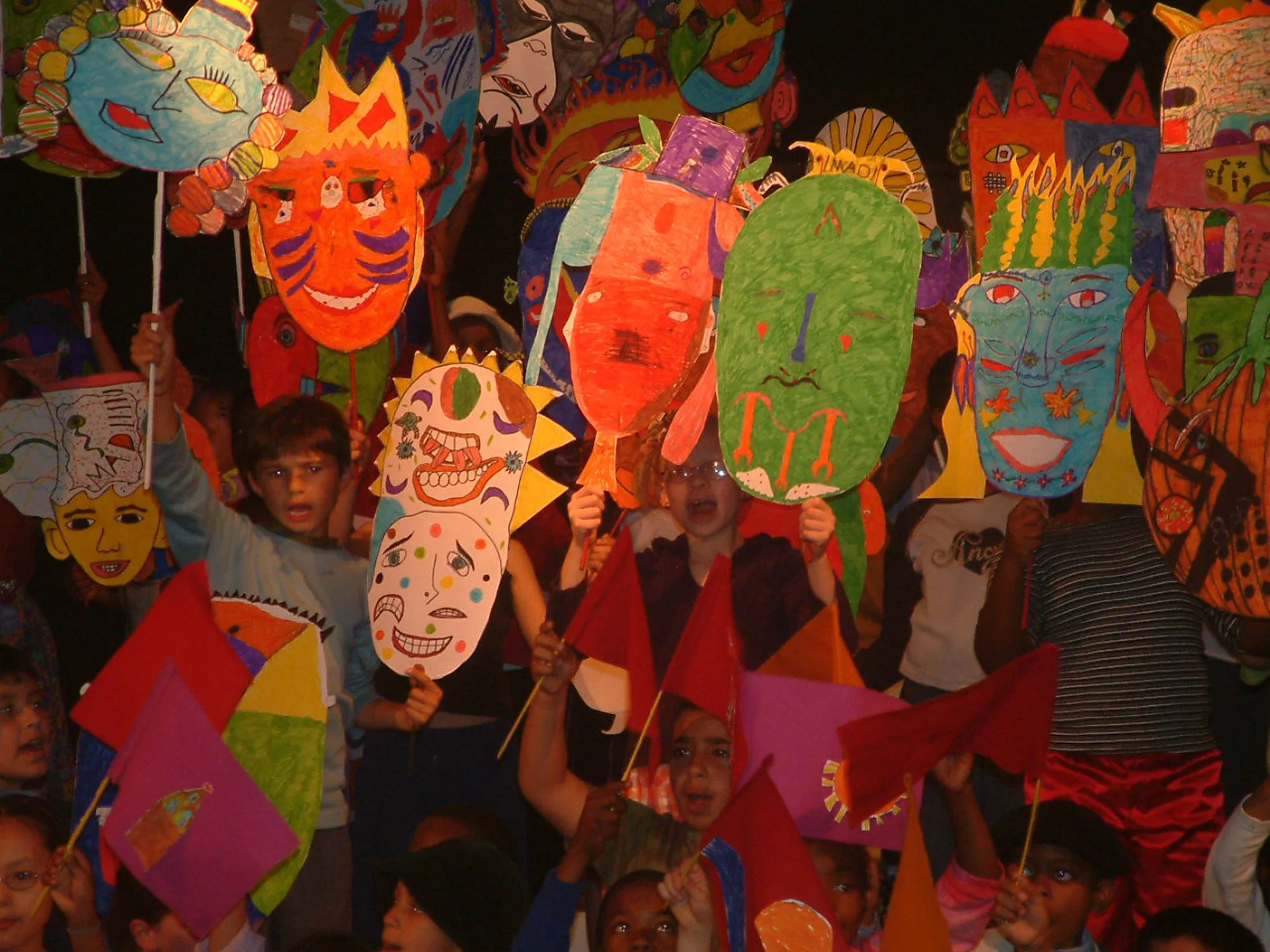 Children holding colorful paper masks and lanterns in a celebration or parade.