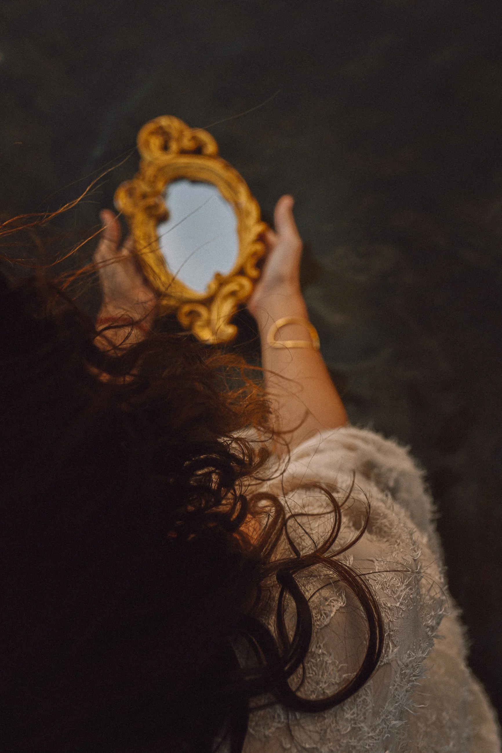 Fotografía cenital de una mujer sosteniendo un pequeño espejo dorado ornamentado entre sus manos, con cabello oscuro y tonos tierra, en el estudio de El Ojo de Venus