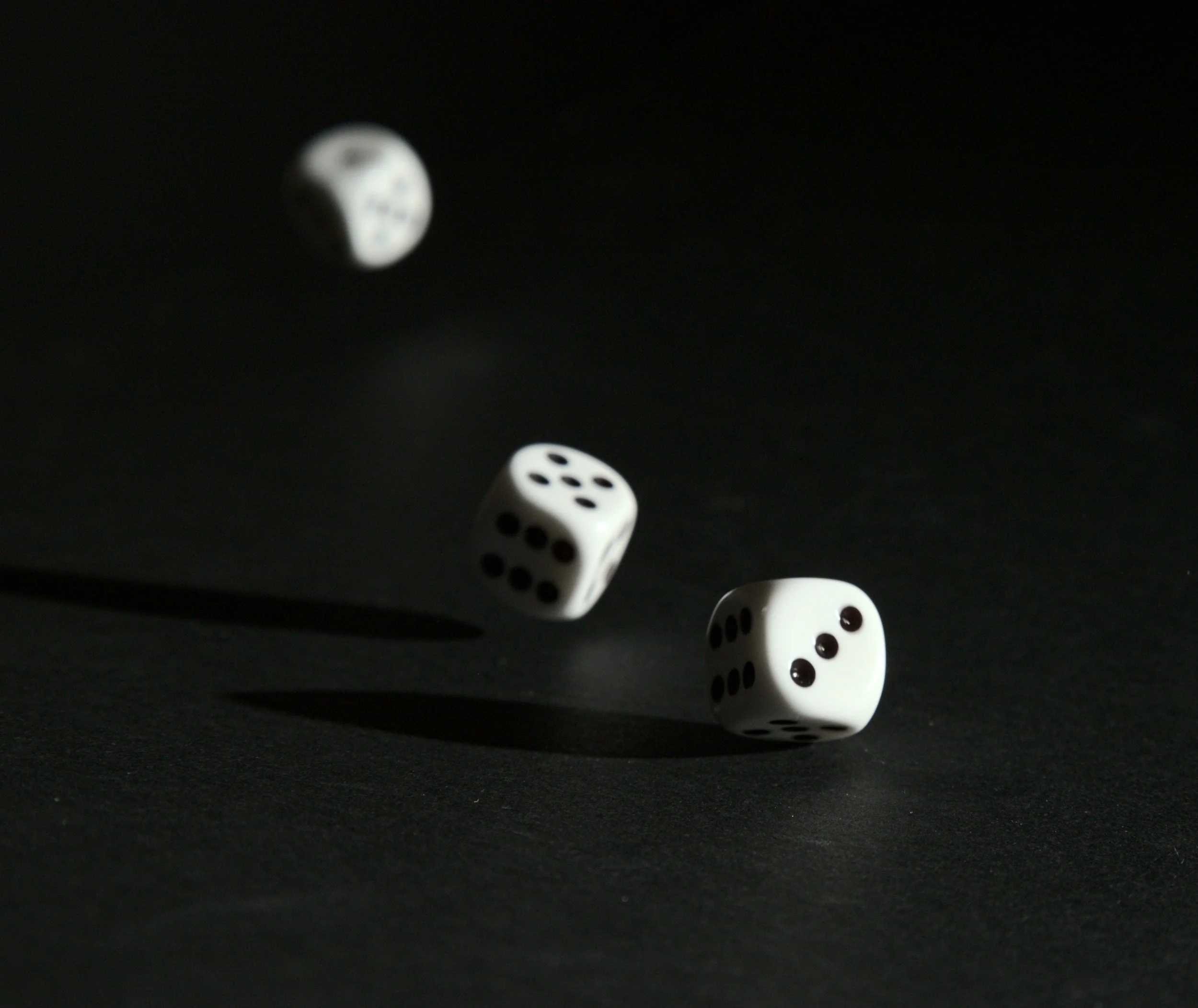 Three white dice with black dots showing 1, 3, and 5 falling on a dark surface, casting shadows, representing 1, 3, and 5 sessions.