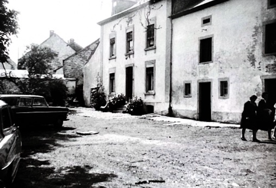 Vieux bâtiment et voitures anciennes dans une rue, deux femmes assises sur un banc, image en noir et blanc, style vintage.