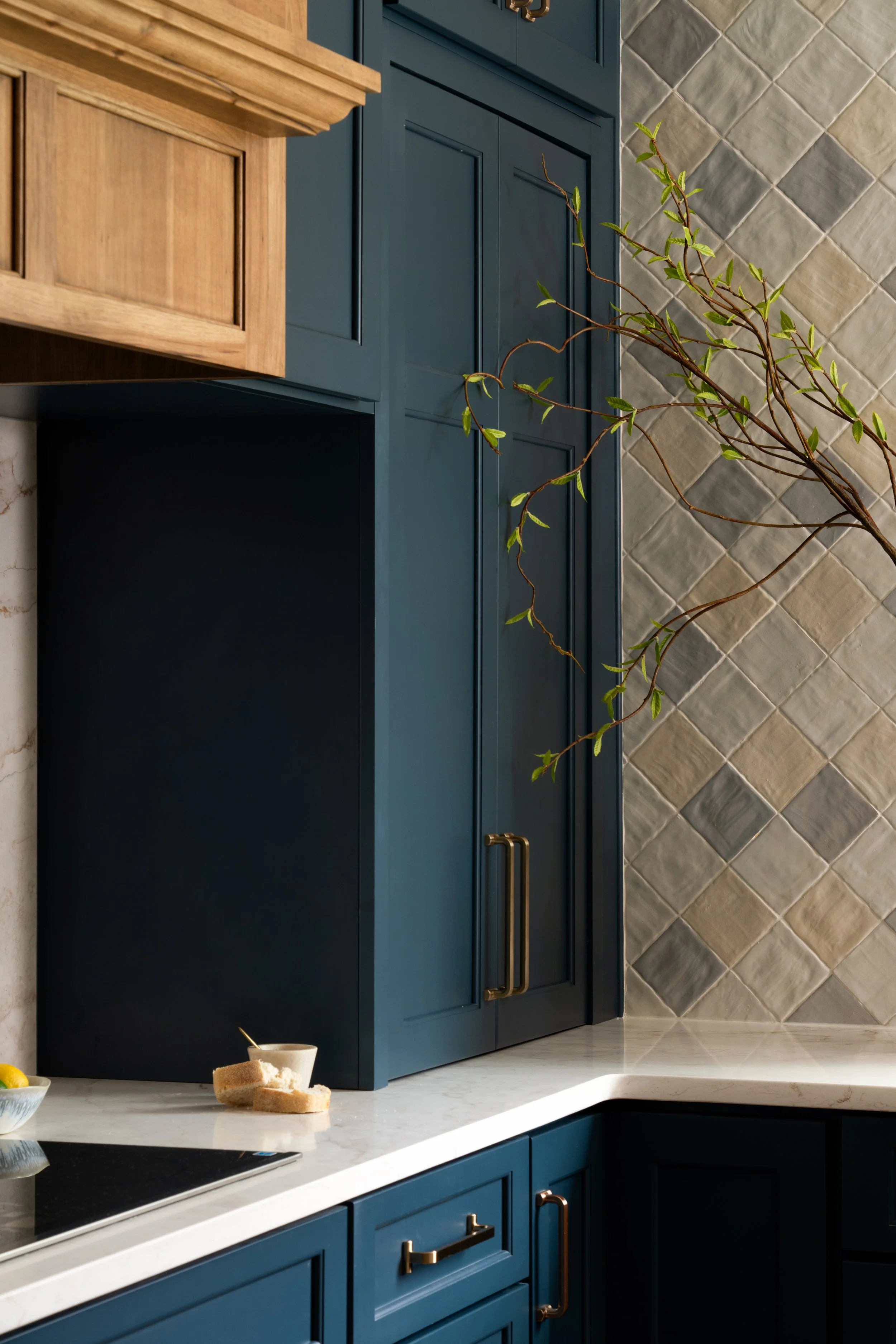 Modern kitchen with blue cabinets and gold handles, beige and gray tiled backsplash, white marble countertop, a small corner of stove and some bread and a lemon on a plate on the counter.