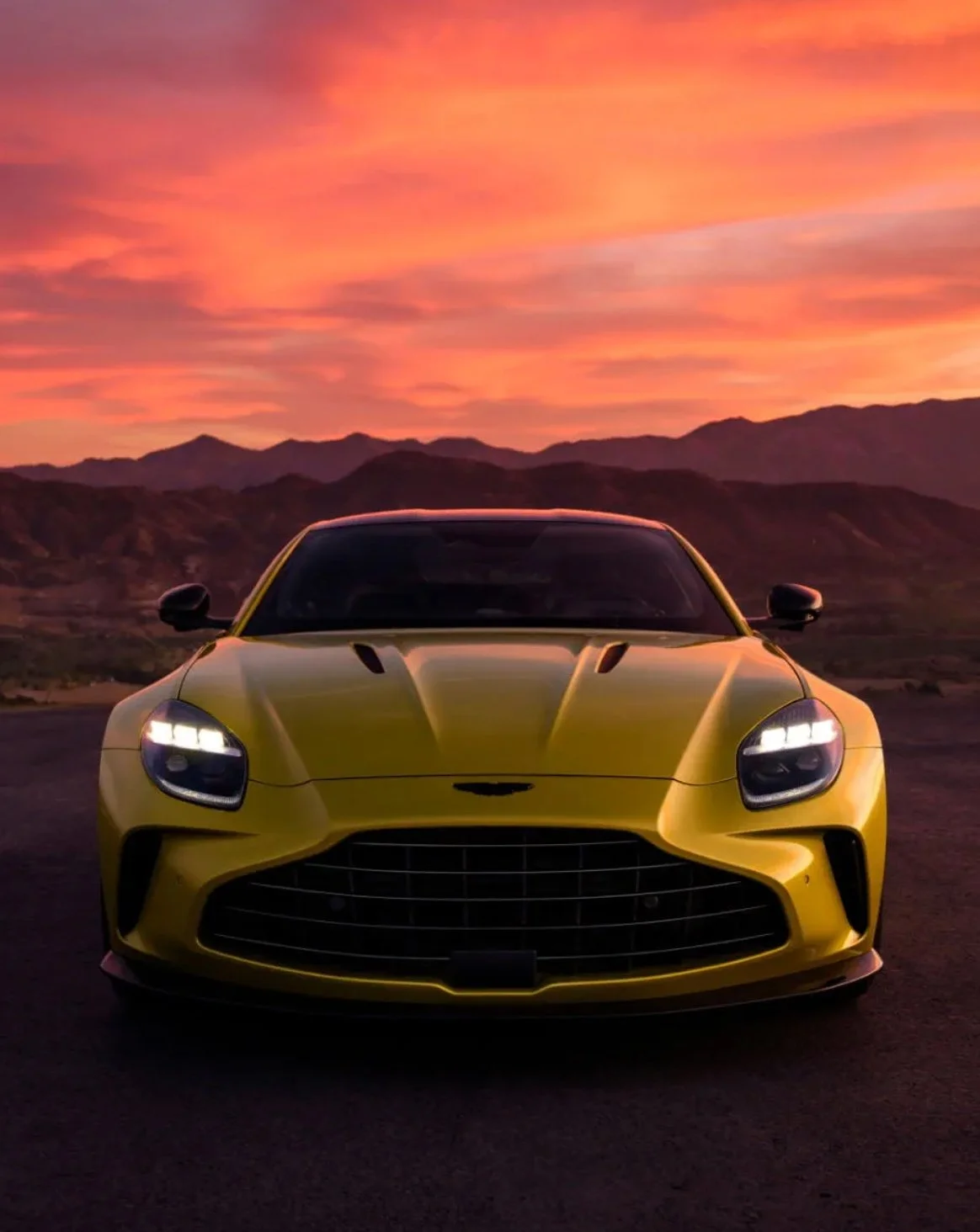 A yellow sports car parked on a road during sunset, with mountains in the background.