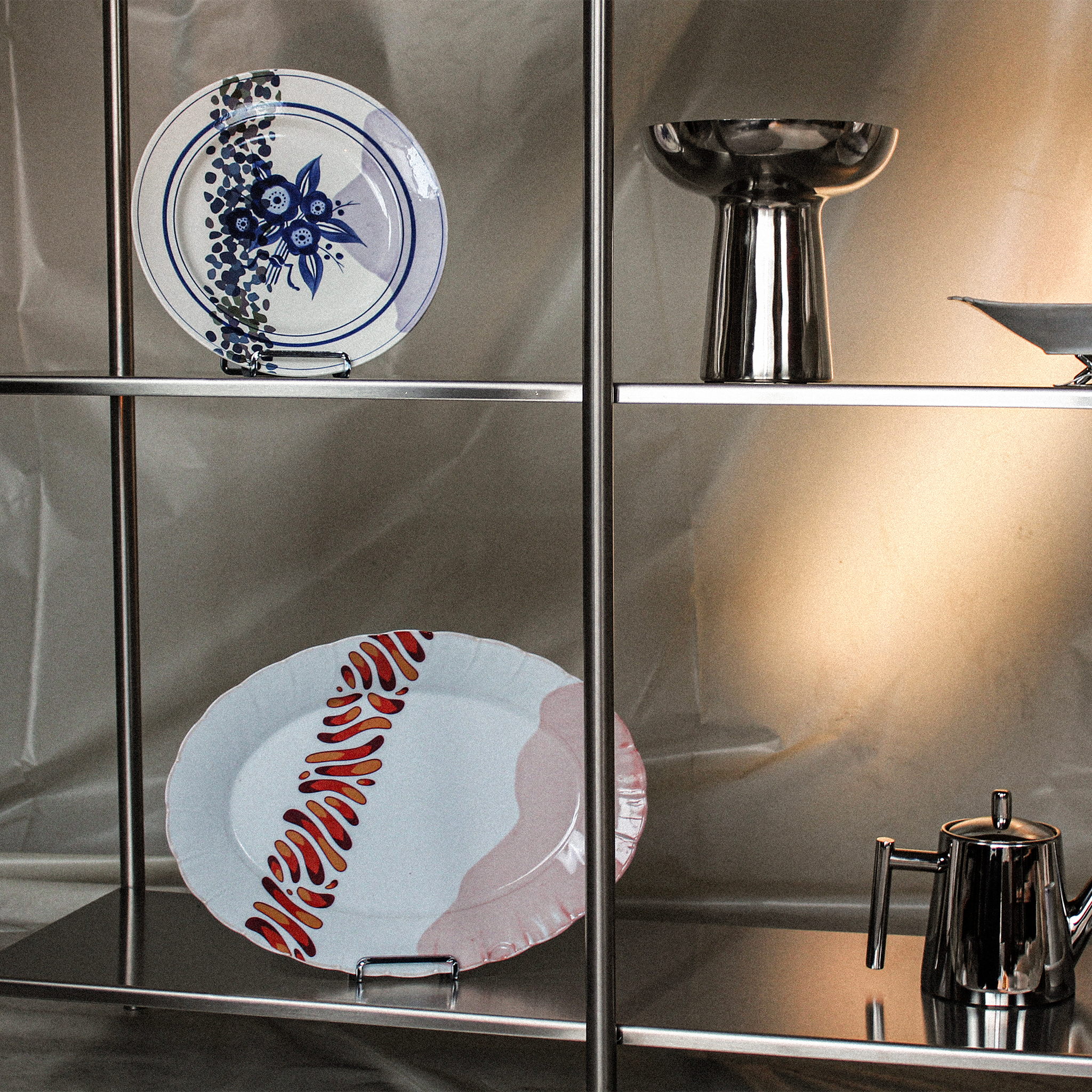 Une étagère en métal avec une assiette en porcelaine décorée de motifs floraux bleus et une base en métal, ainsi qu'un objet métallique arrondi.
