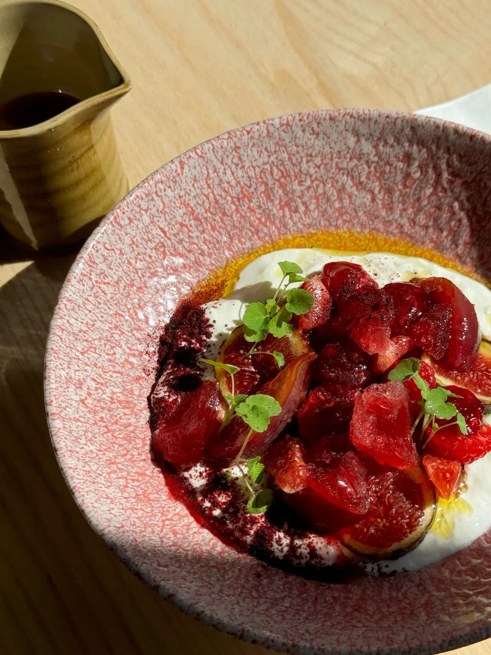 Assiette en céramique upcyclée rose et blanche, dressée avec des figues, des fruits rouges, du yaourt crémeux et des herbes fraîches, sur une table en bois.