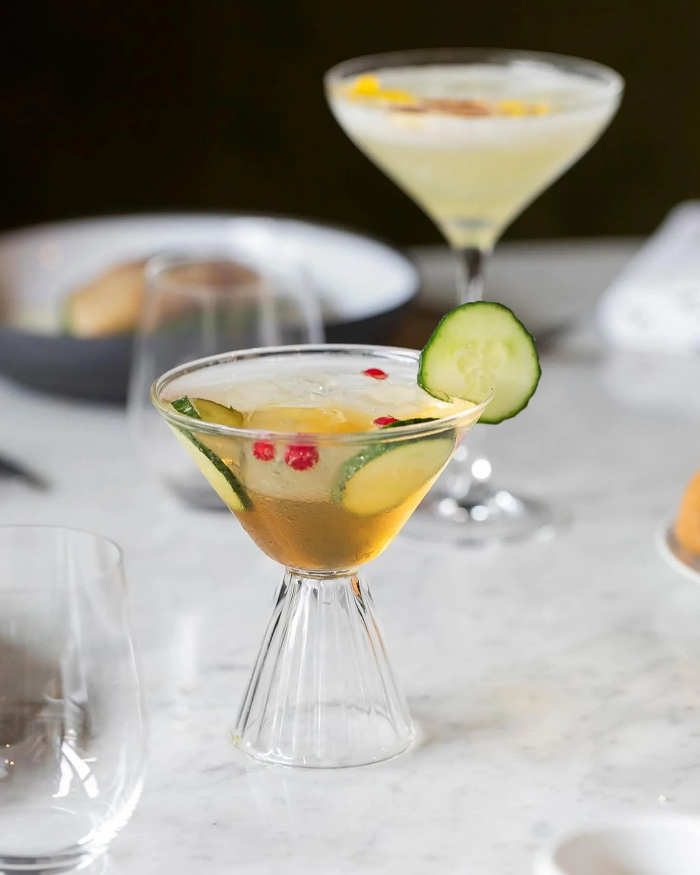 Un cocktail dans un verre transparent conique.  Le liquide est ambré et le verre est décoré avec des rondelles de concombre.