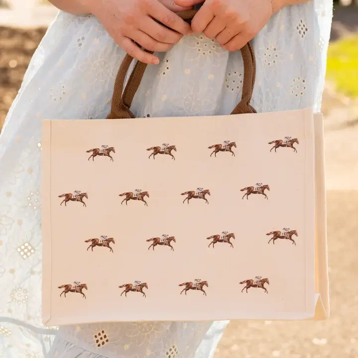 Woman carrying a Running Horse Tote Bag featuring a horse racing pattern