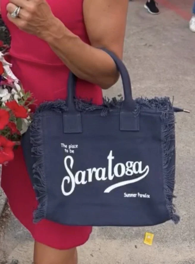 Woman carrying a navy Saratoga Summer Paradise Fringed Tote at Saratoga Race Course