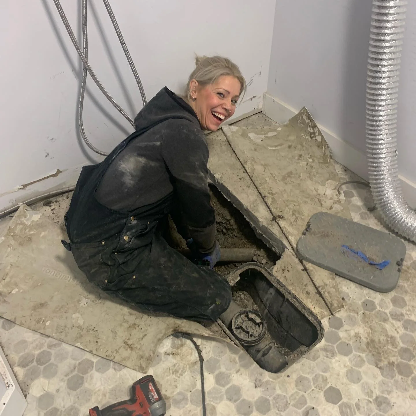 Person in overalls working on plumbing in a partially removed floor