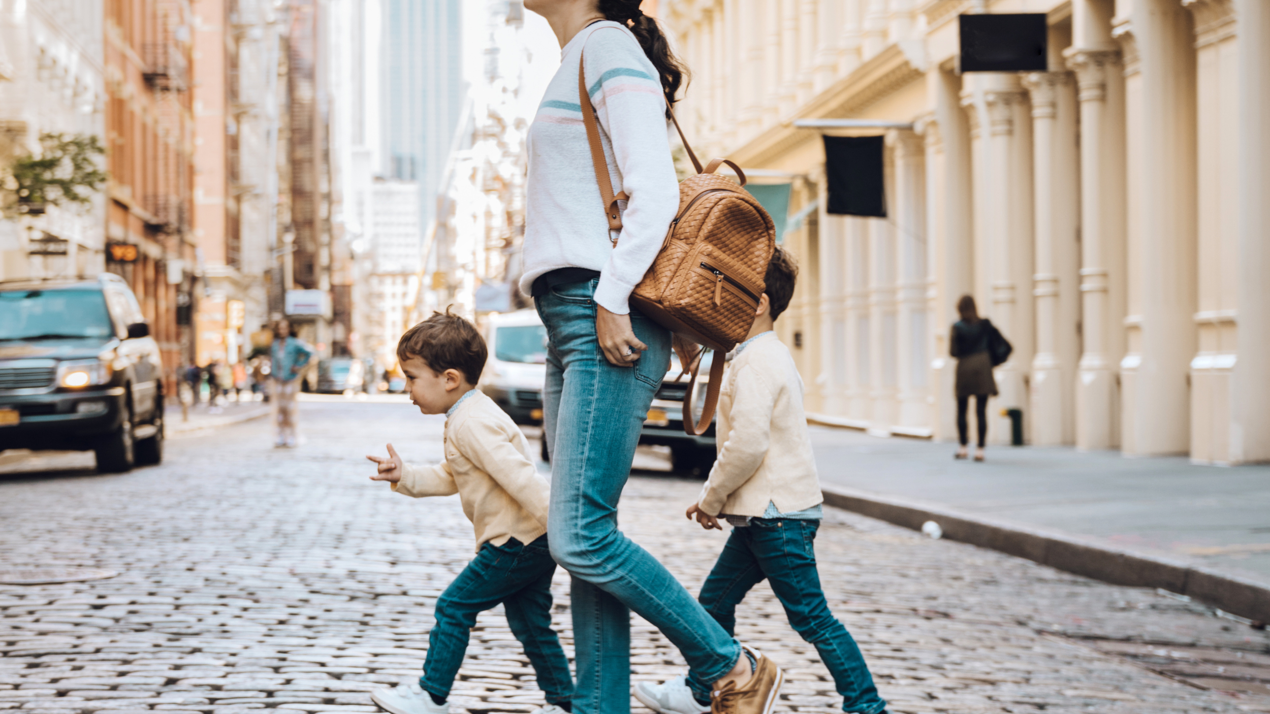 Mother walking with two children in matching outfits across a busy city street