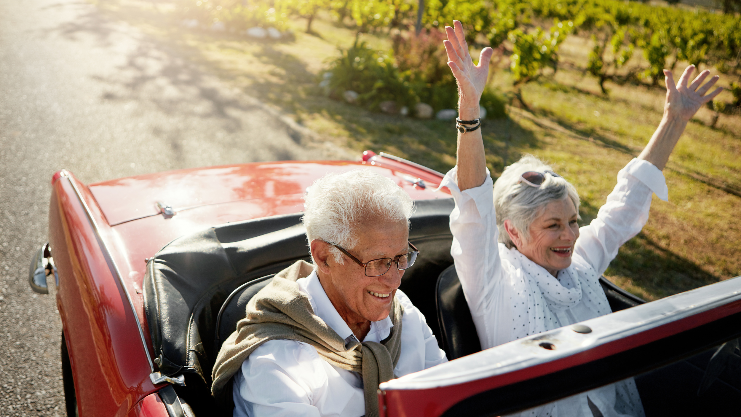 Happily retired couple on a drive in a red convertible car with the top down