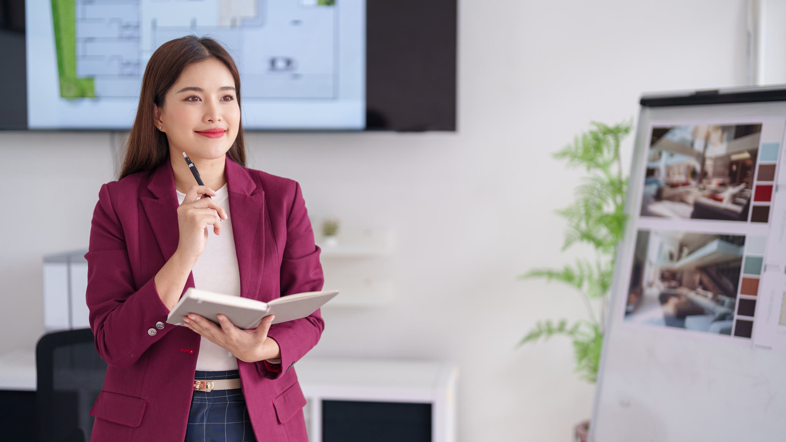 Professional woman holding a notebook and pen while reviewing design boards and planning projects in a modern office.
