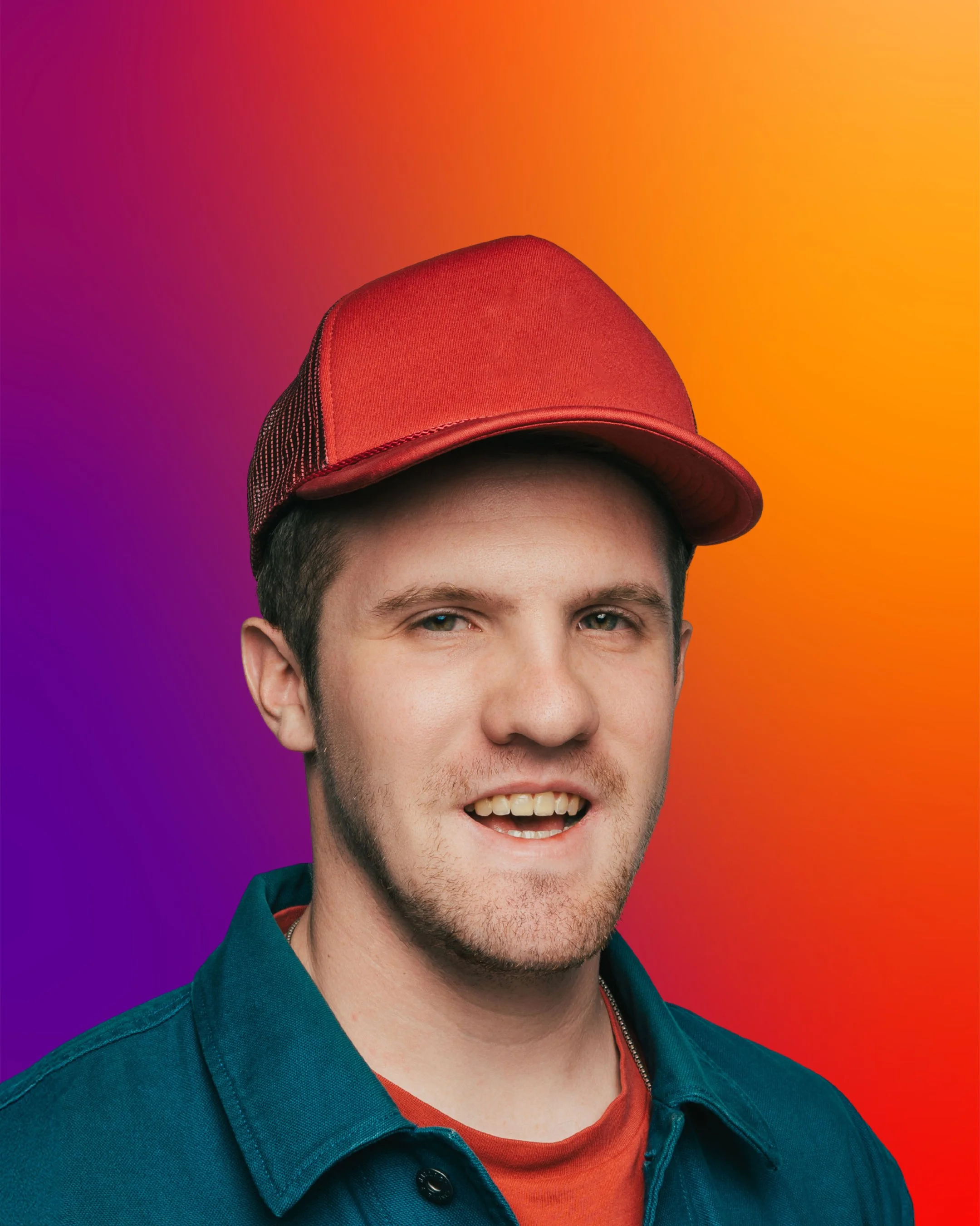 A young man wearing a red baseball cap and a teal jacket, smiling with a colorful gradient background.