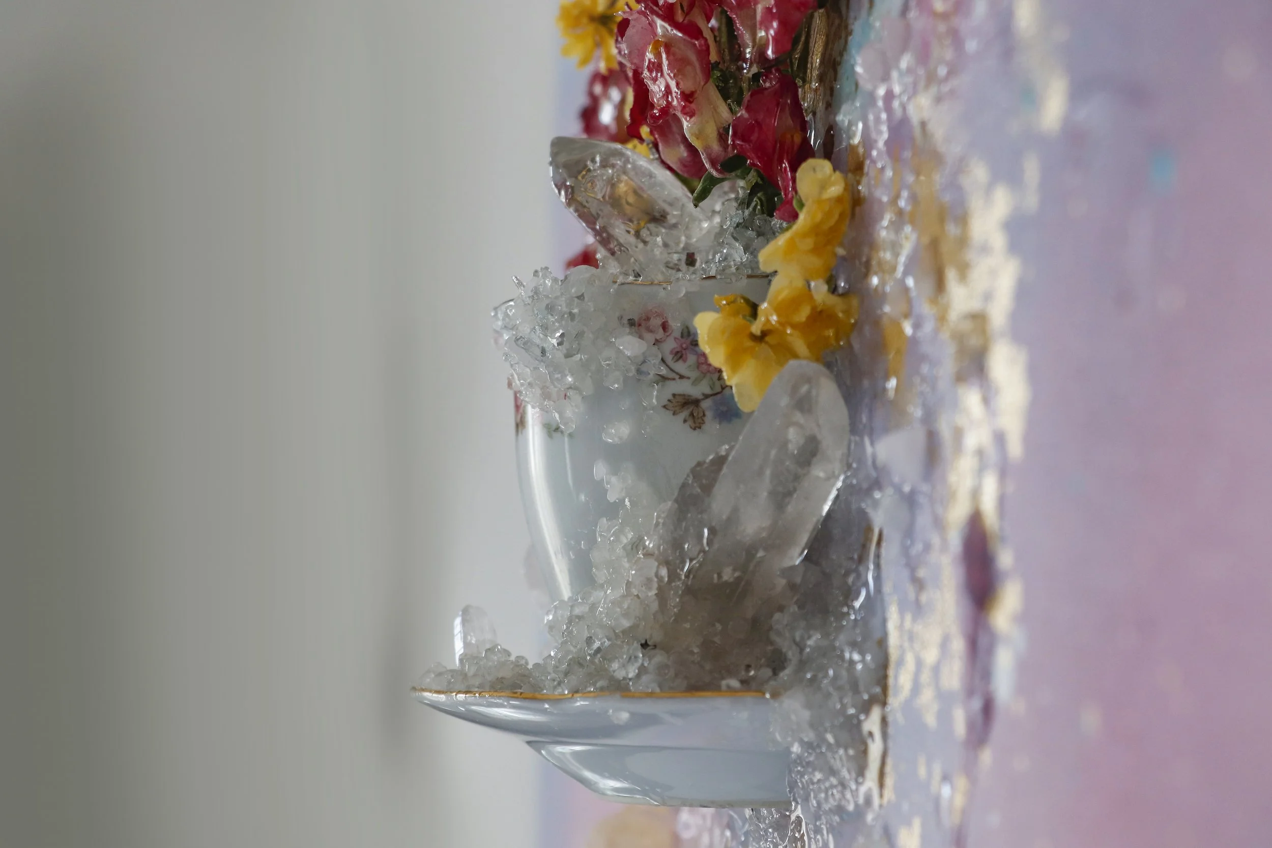 Detail photo of a tea cup covered in quartz crystals and pink and yellow flowers (snap dragons and mini roses)