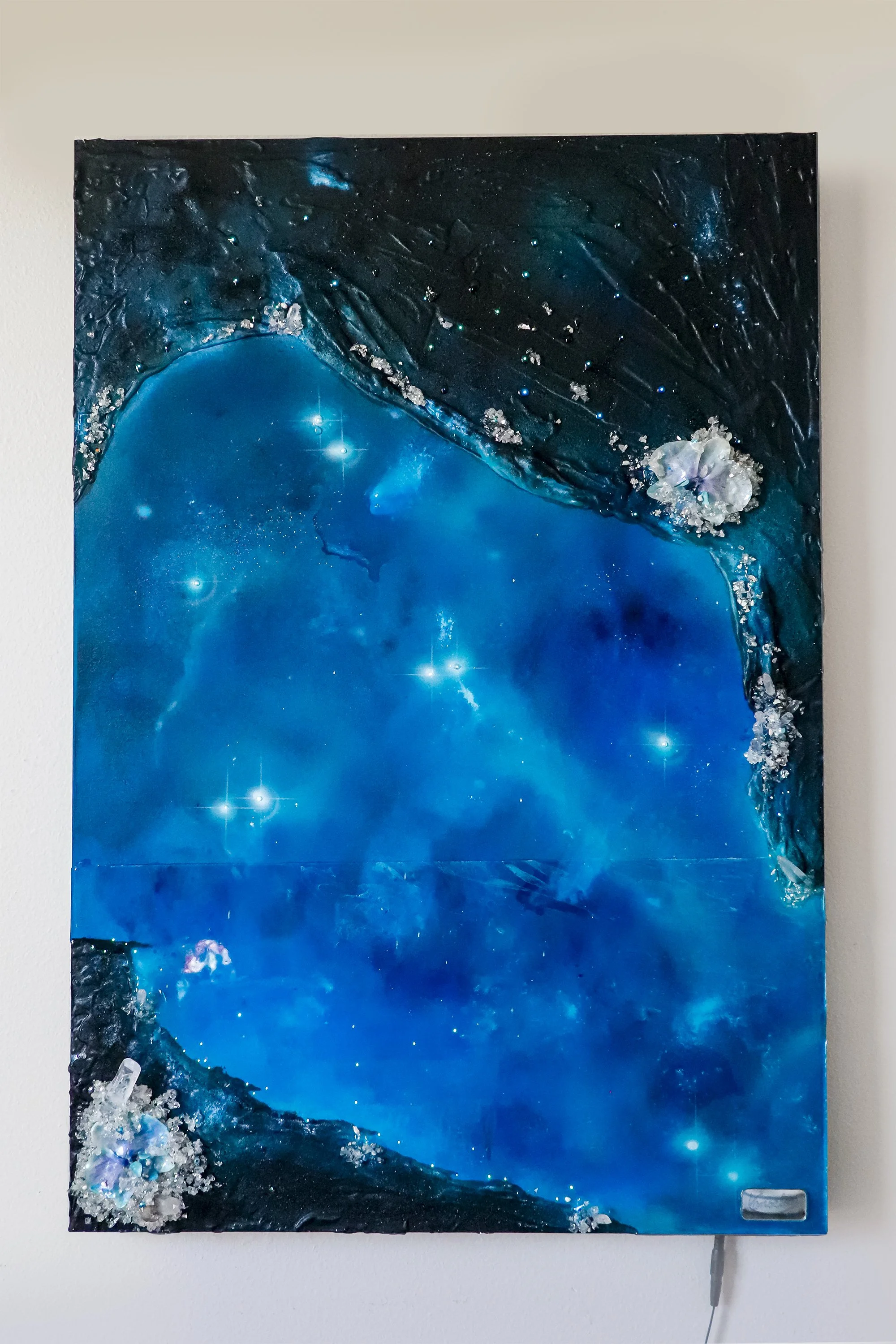 Blue abstract wall art hanging on wall, with orchid botanicals, quartz crystals and resin