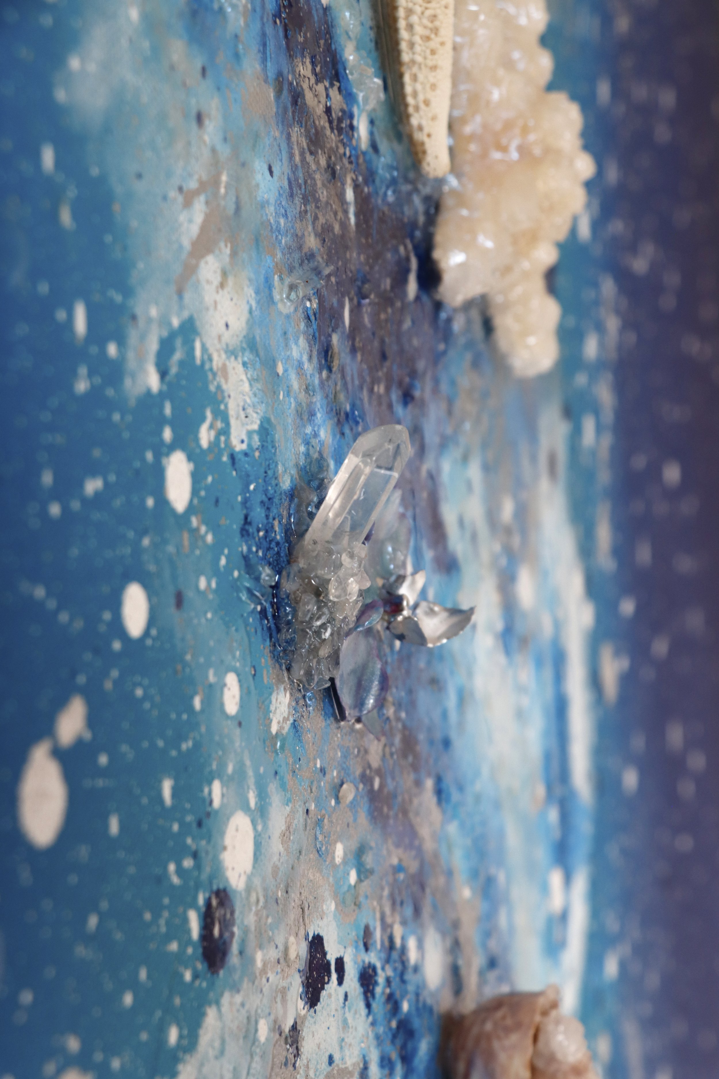 detail photo of quartz crystal point and orchid on a large blue abstract painting